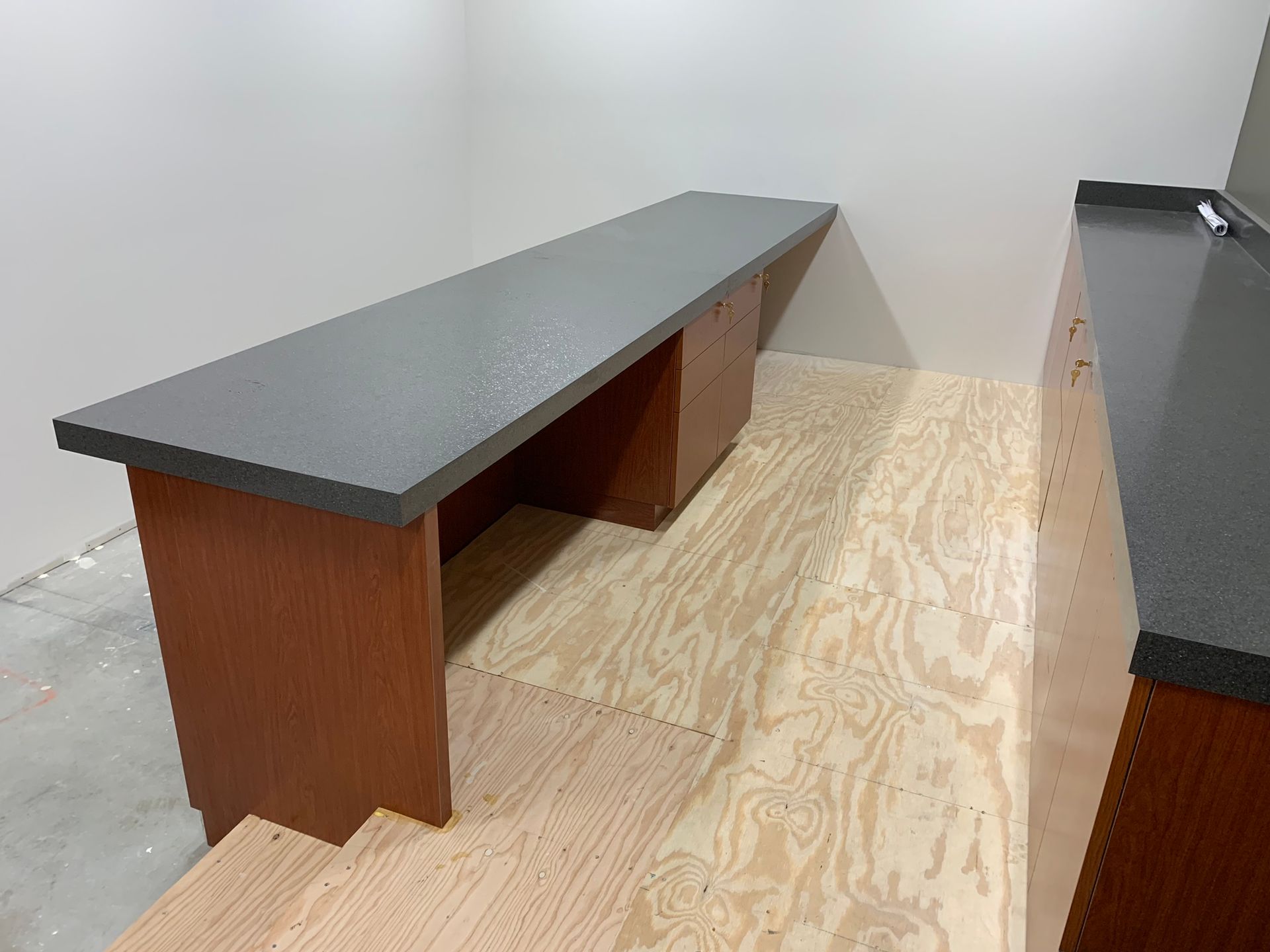 Long wooden desk with a gray countertop in a room under construction.
