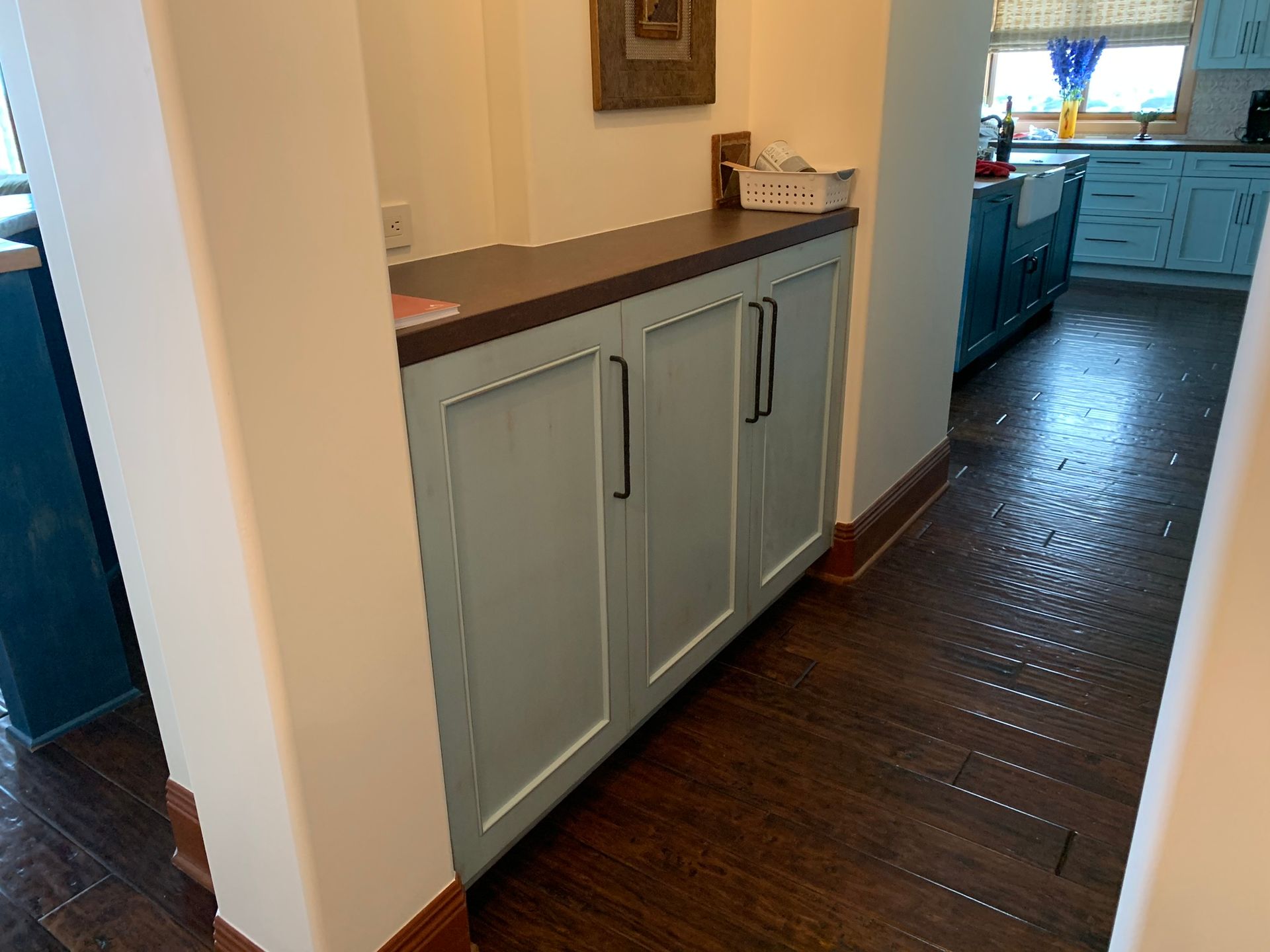 Light blue cabinet with dark countertop in a kitchen. Dark wood flooring.