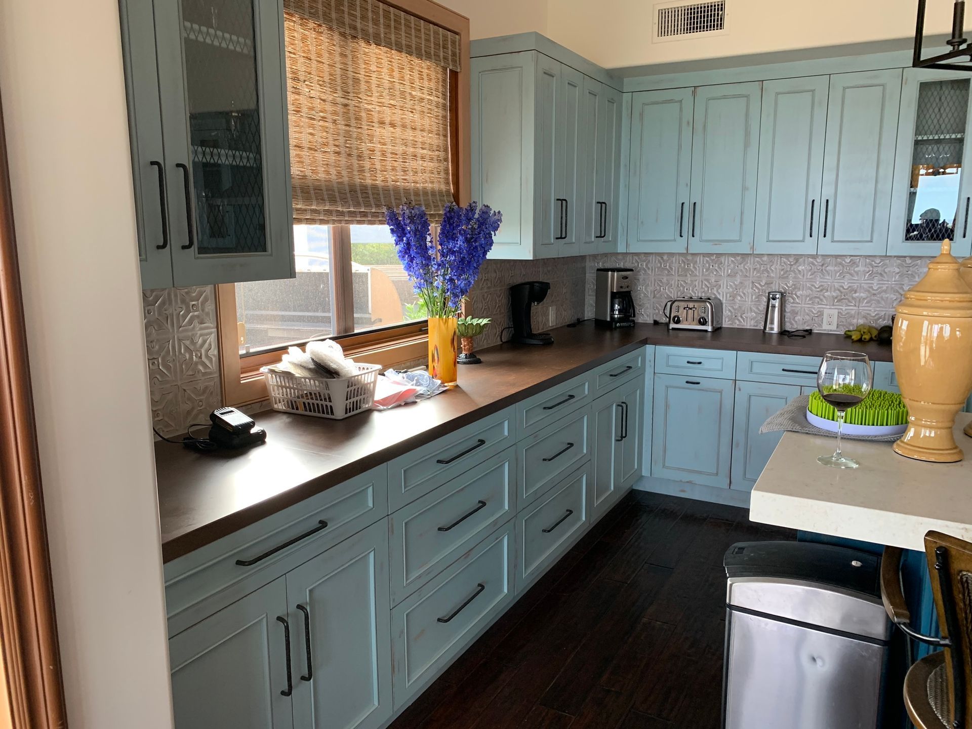 Light blue kitchen cabinets with dark countertops, wood floors, and decorative backsplash.