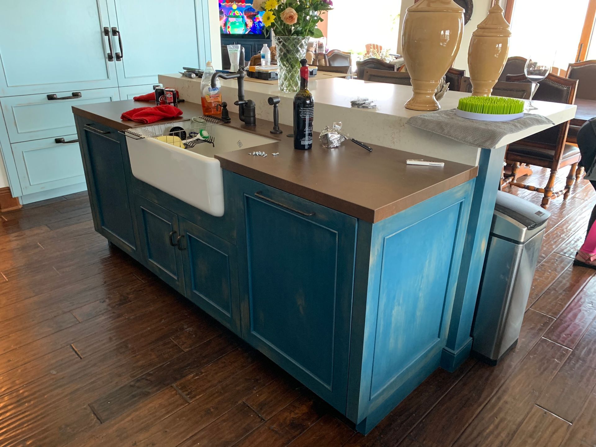 Blue kitchen island with a farmhouse sink, wooden countertop, and wine bottle.
