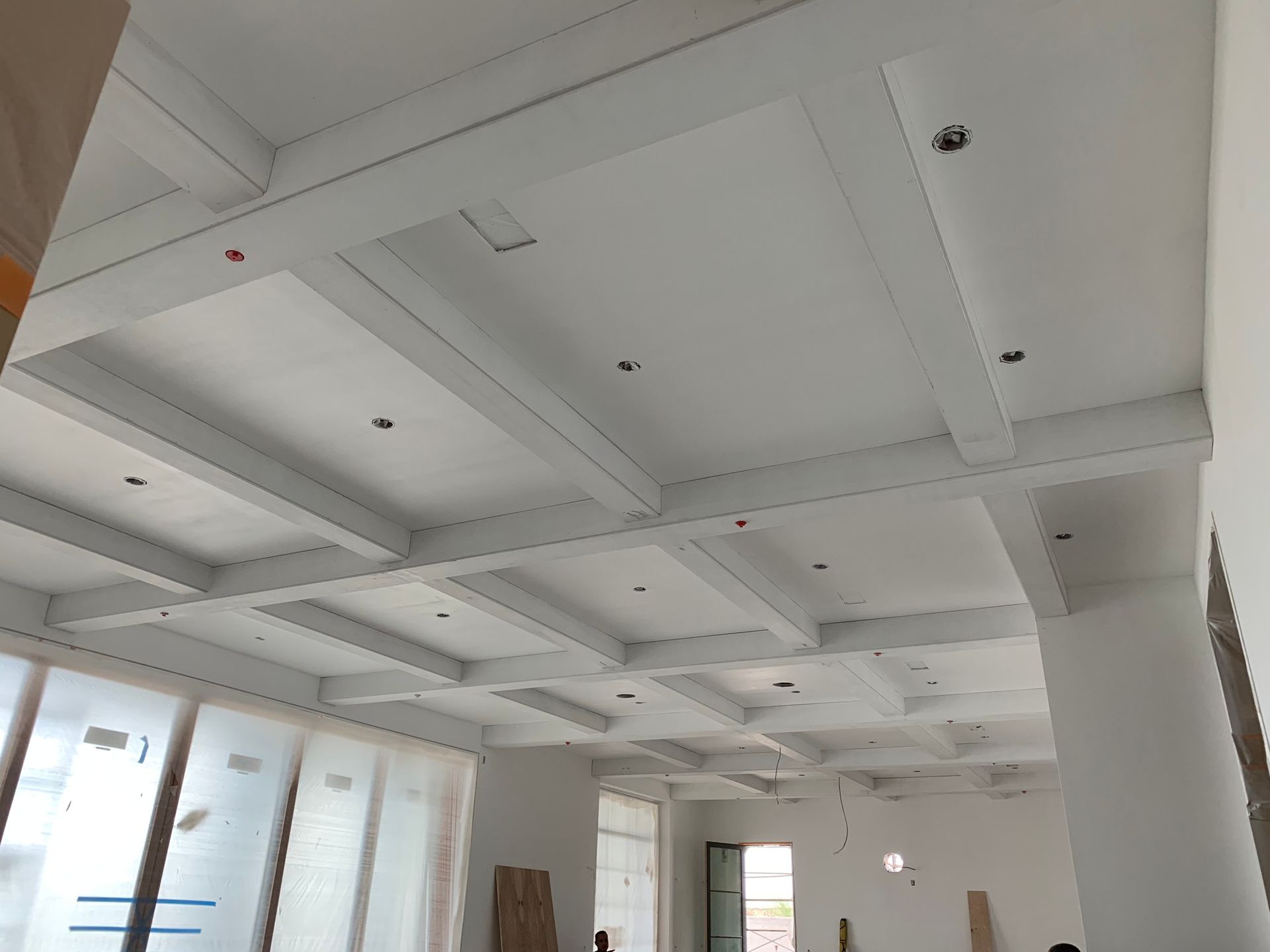 White coffered ceiling with recessed lighting in a light-filled room.