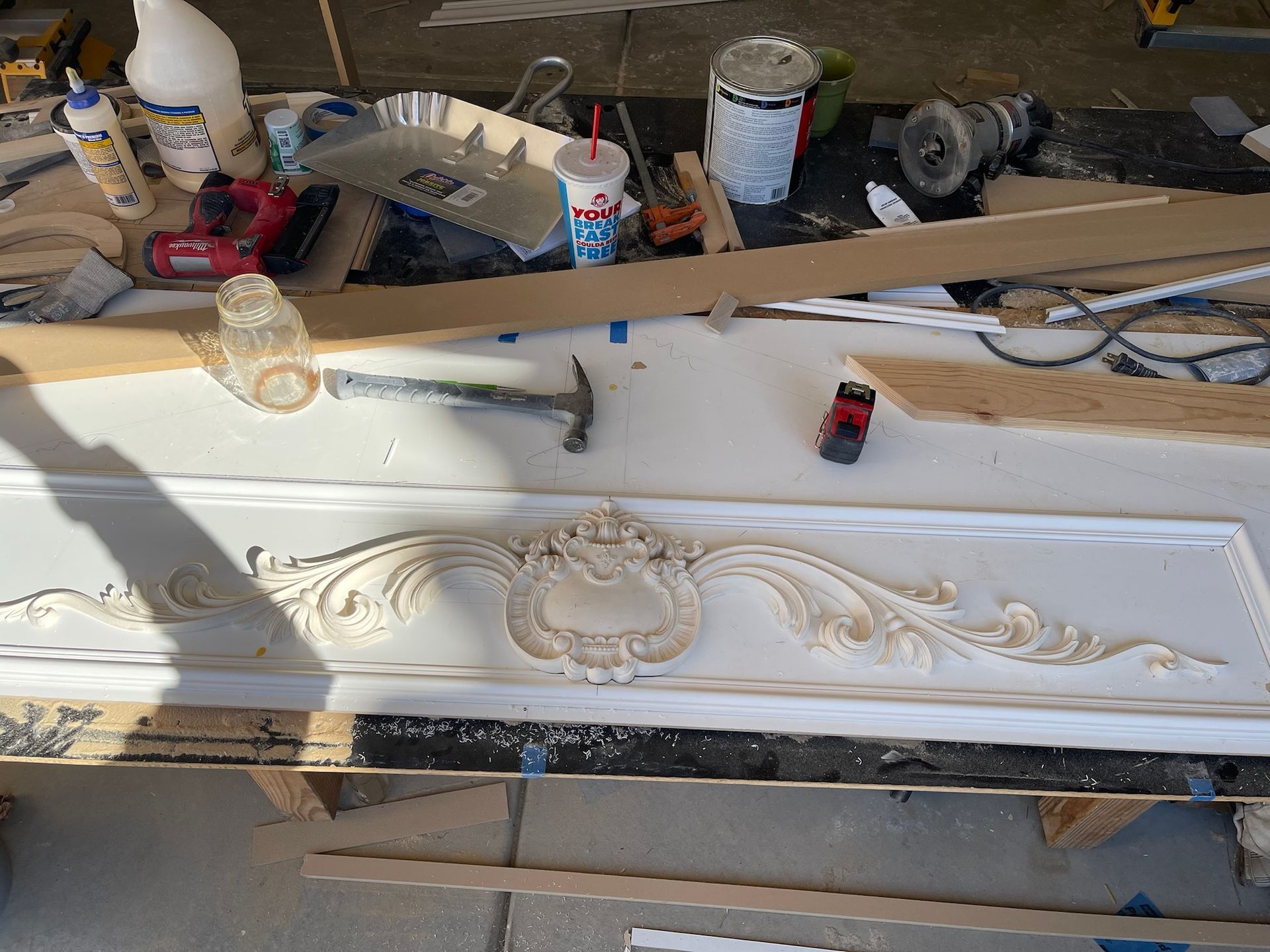 A detailed ornate wooden decorative panel with tools, wood, and supplies on a work surface.