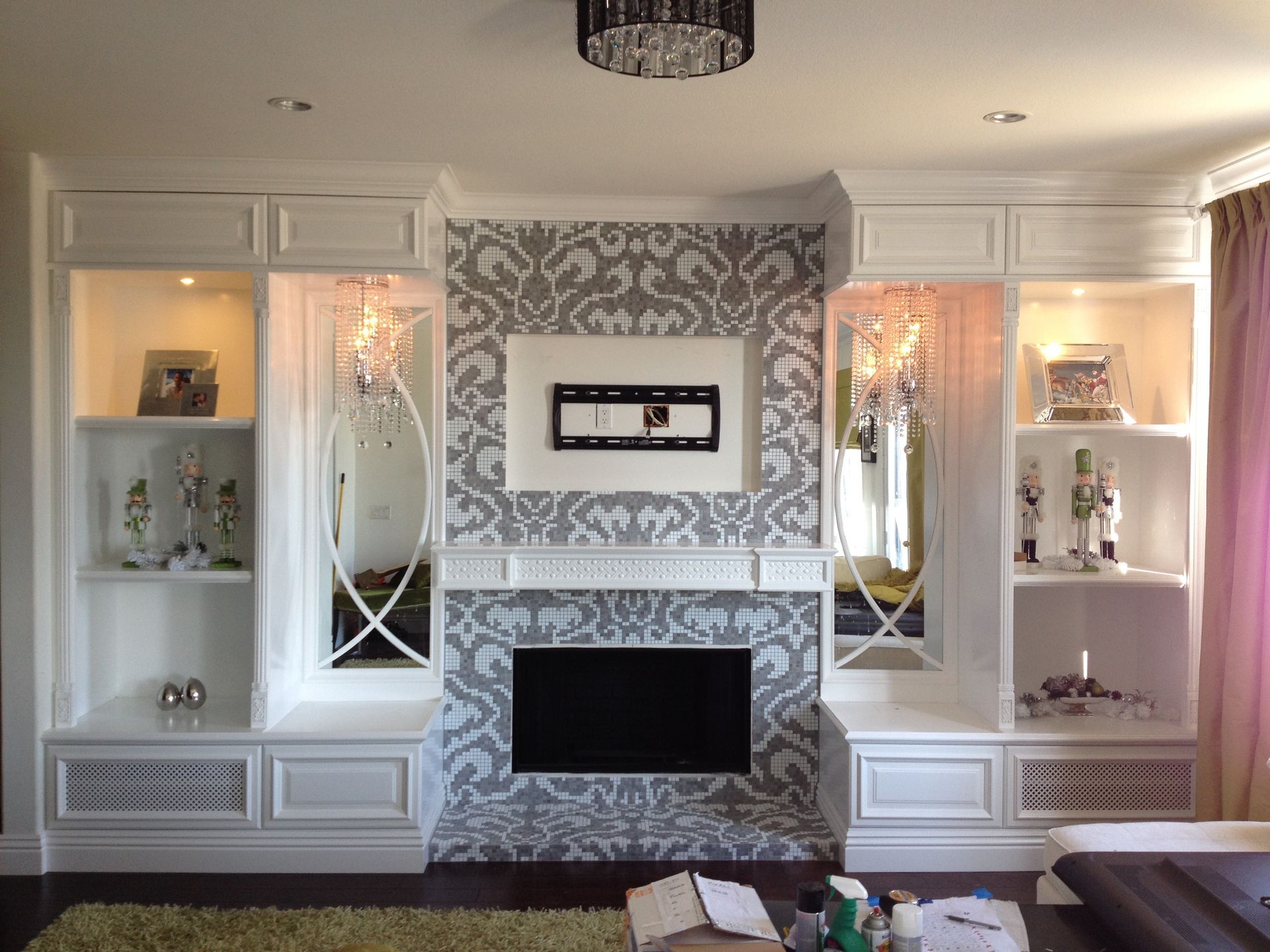 Built-in white media center with fireplace, TV, and display shelves, featuring mirrored accents and gray patterned wallpaper.