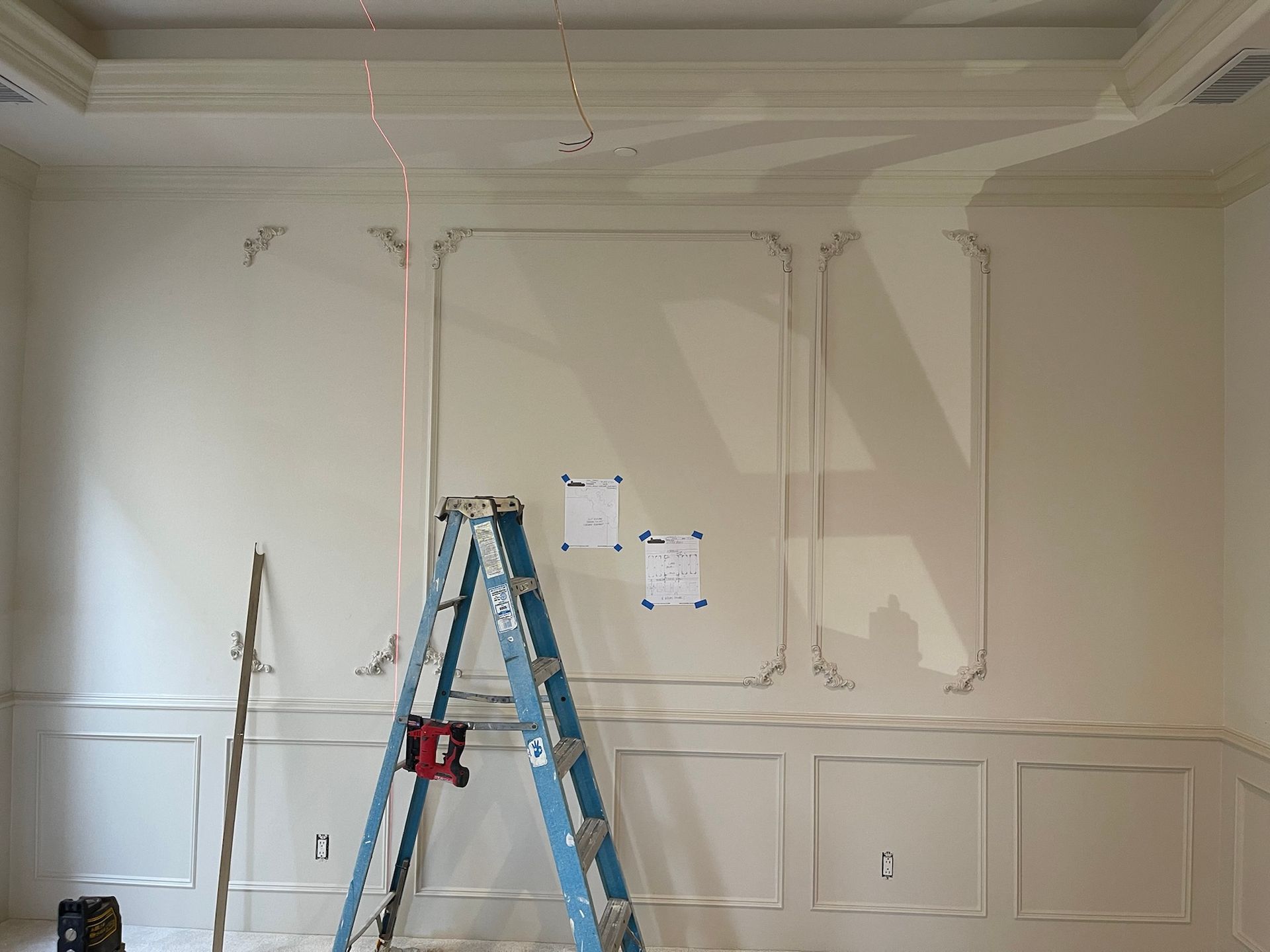 Interior room with wall molding under construction, blue ladder, papers on the wall.
