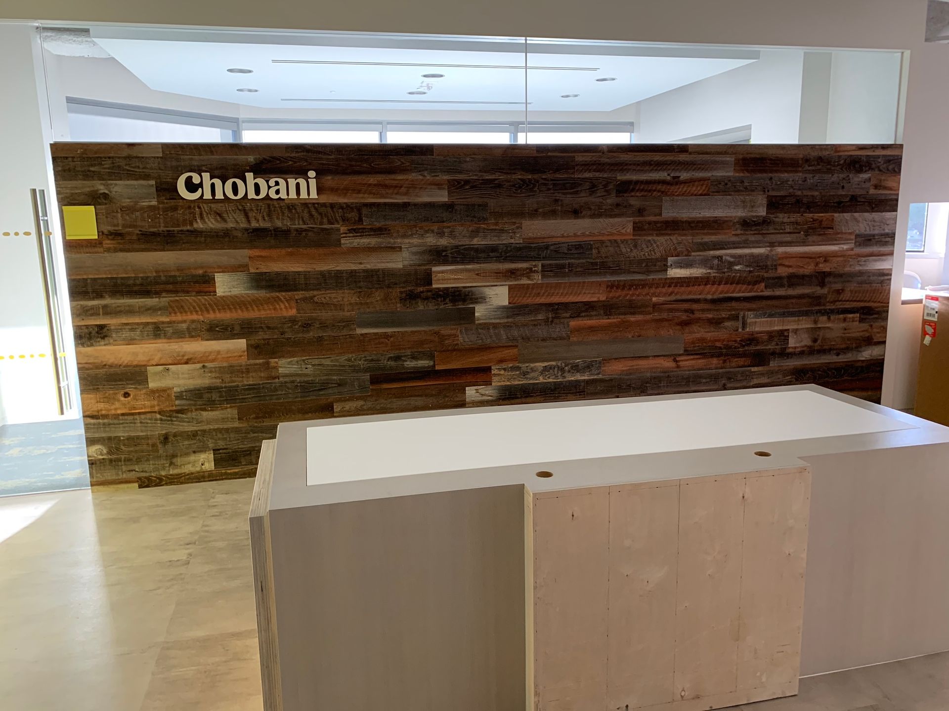 Chobani logo on a wood-paneled wall above a white reception desk. Office interior.