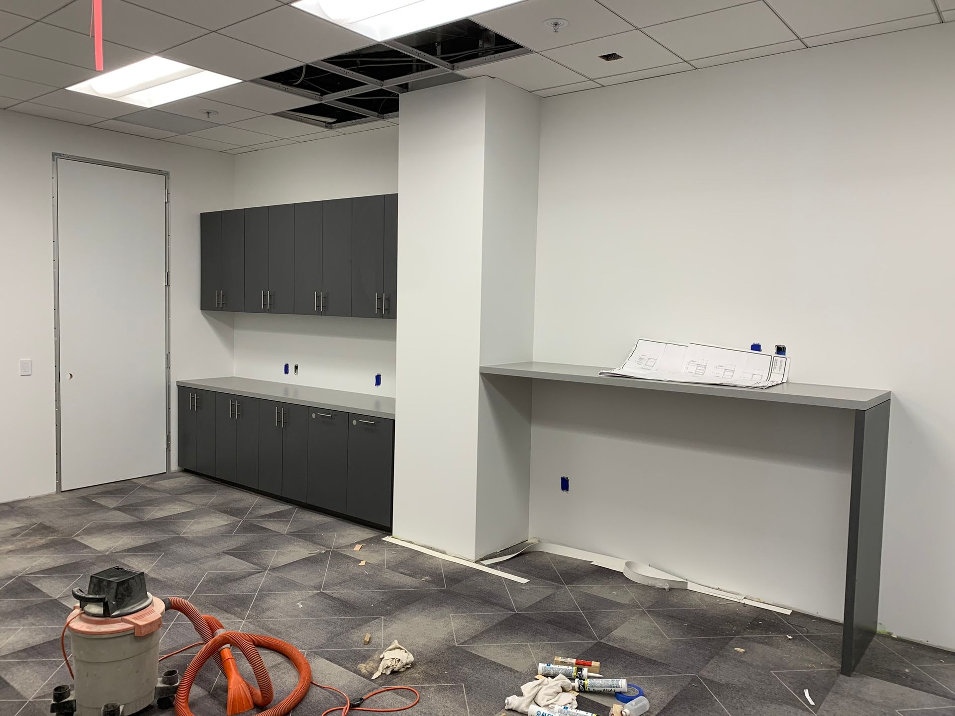 Office space under construction with grey cabinets, counter, and unfinished ceiling.