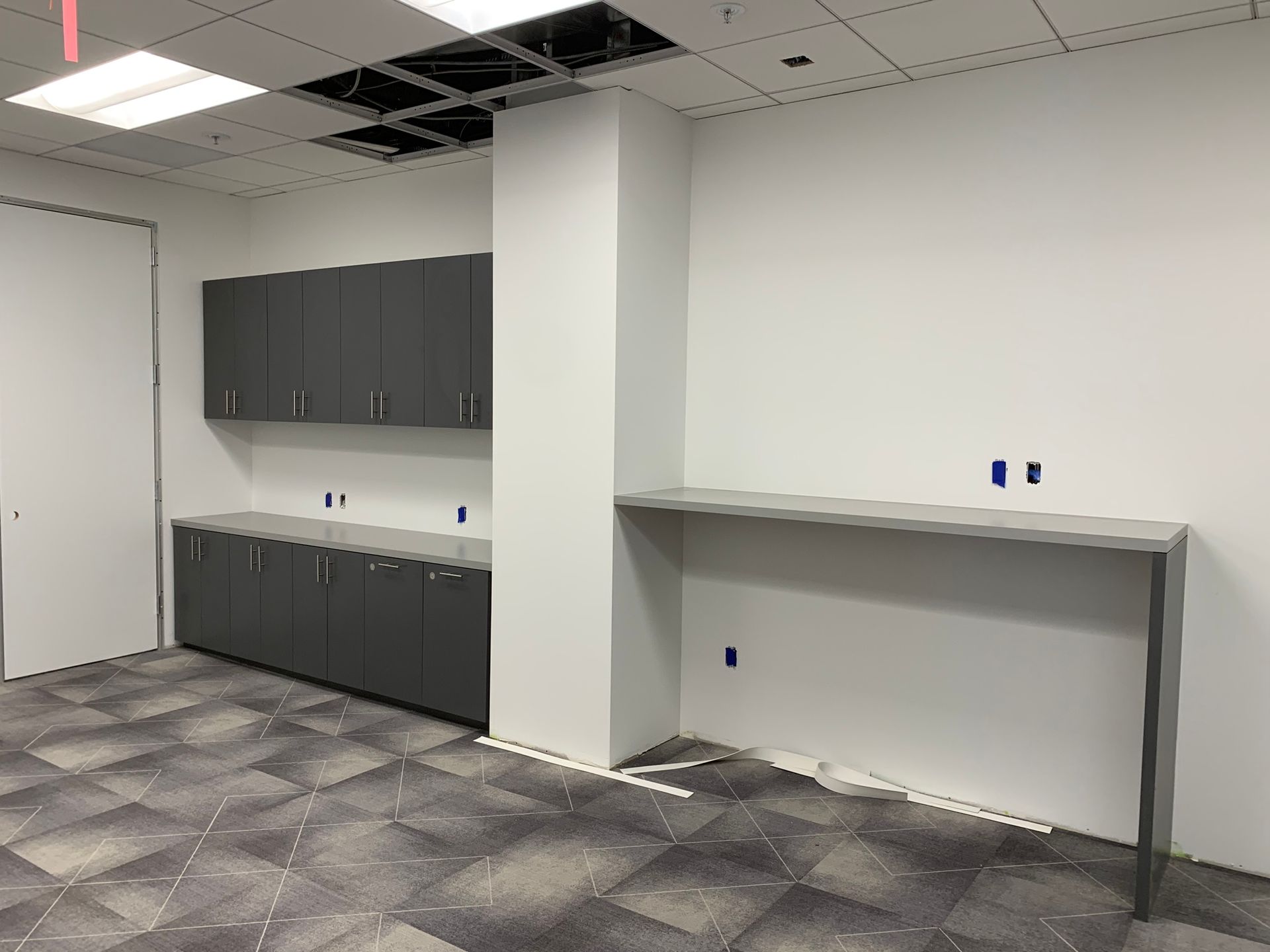 A room under construction with gray cabinets, countertop, and a white pillar; gray and white patterned floor.