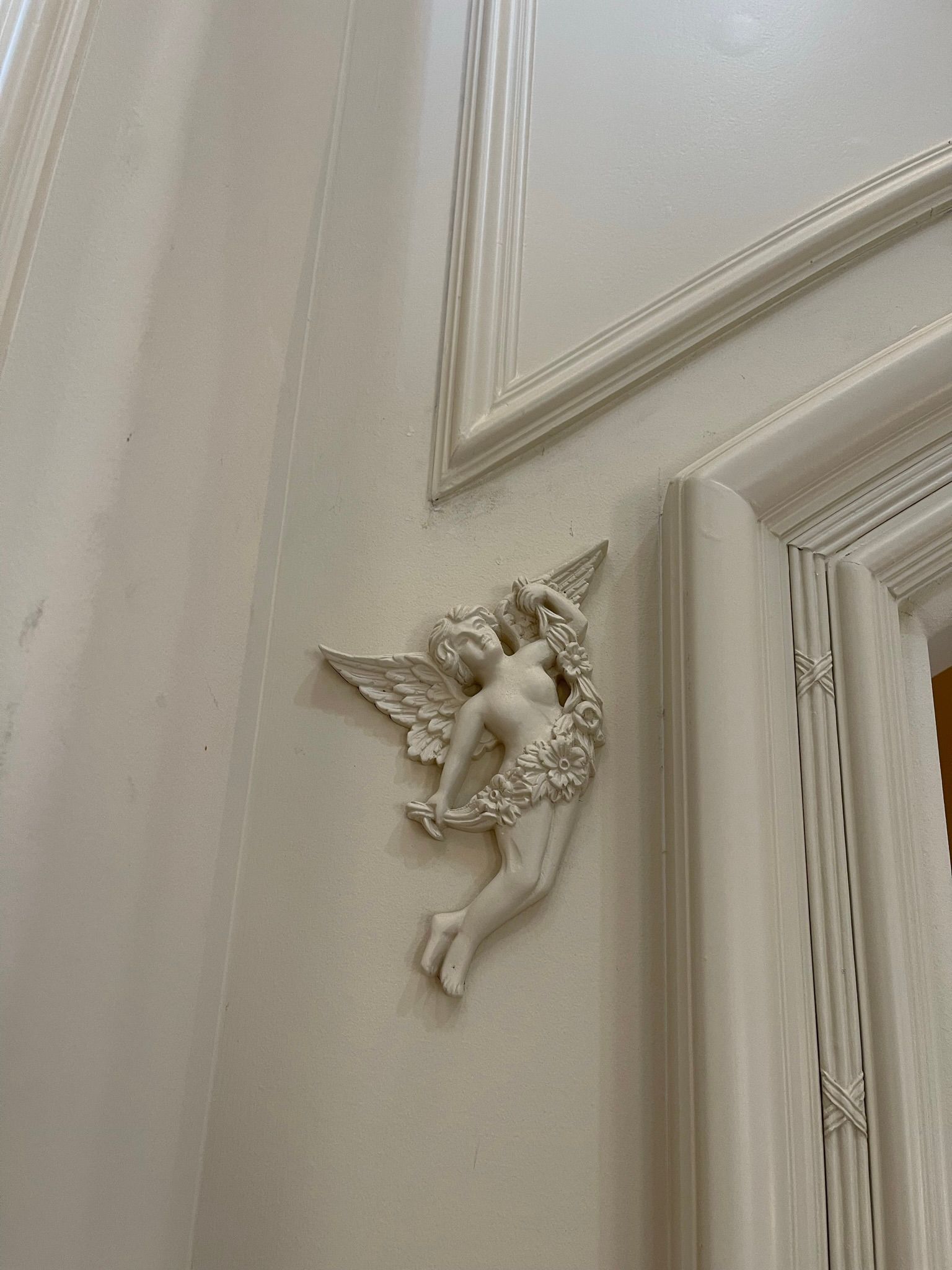 White relief sculpture of an angel with wings on a white door frame.