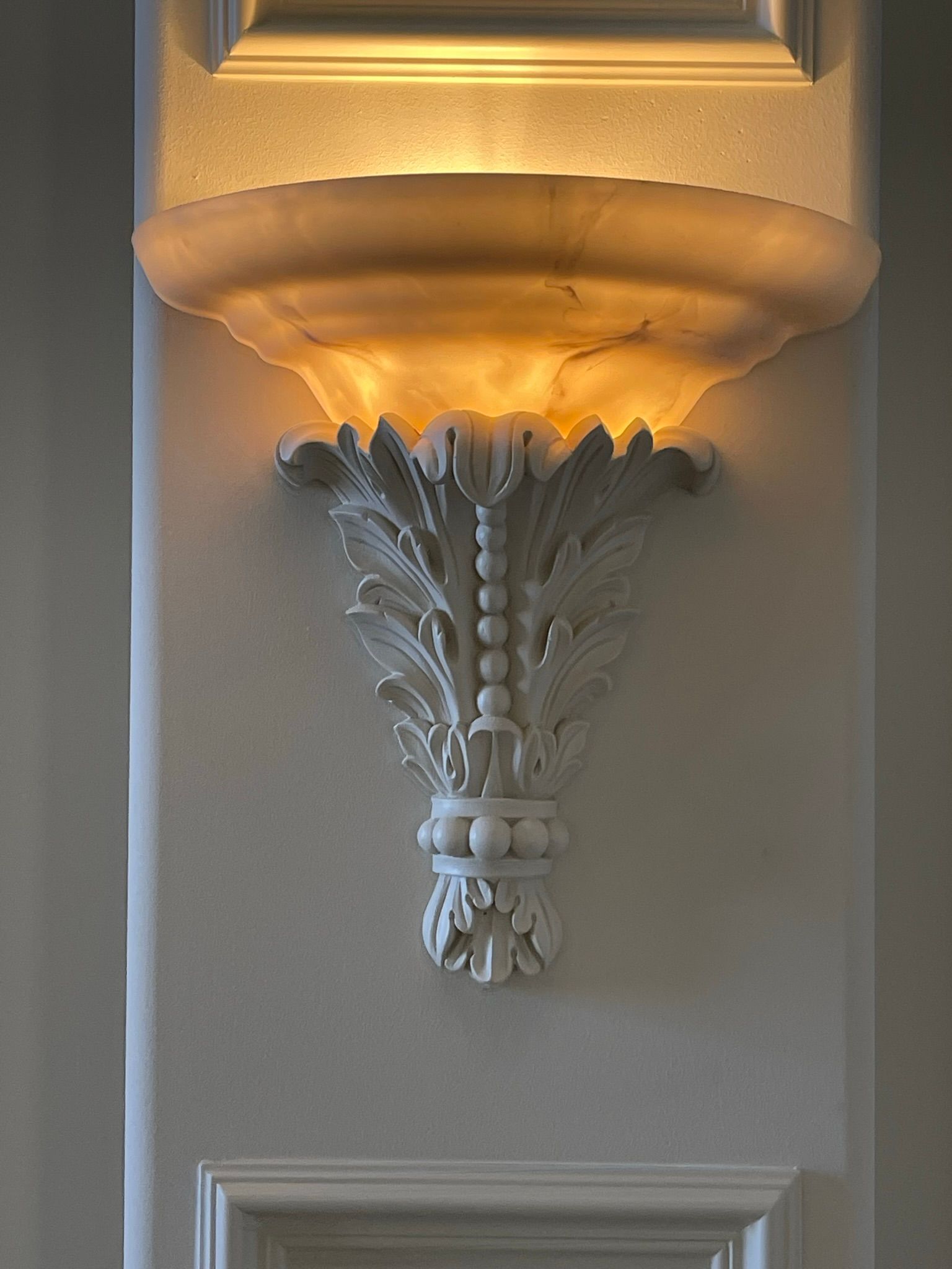 White ornate wall sconce with a glowing, bowl-shaped light.