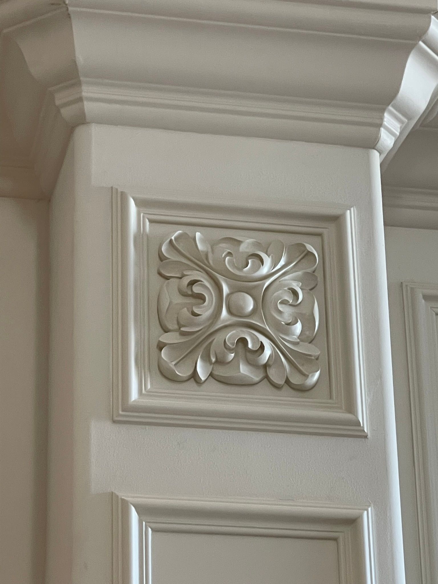 White decorative square panel with carved floral design and surrounding molding.