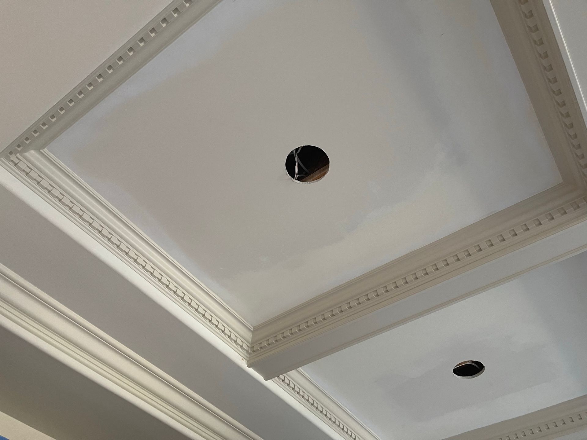 White ceiling with decorative molding and two round holes.