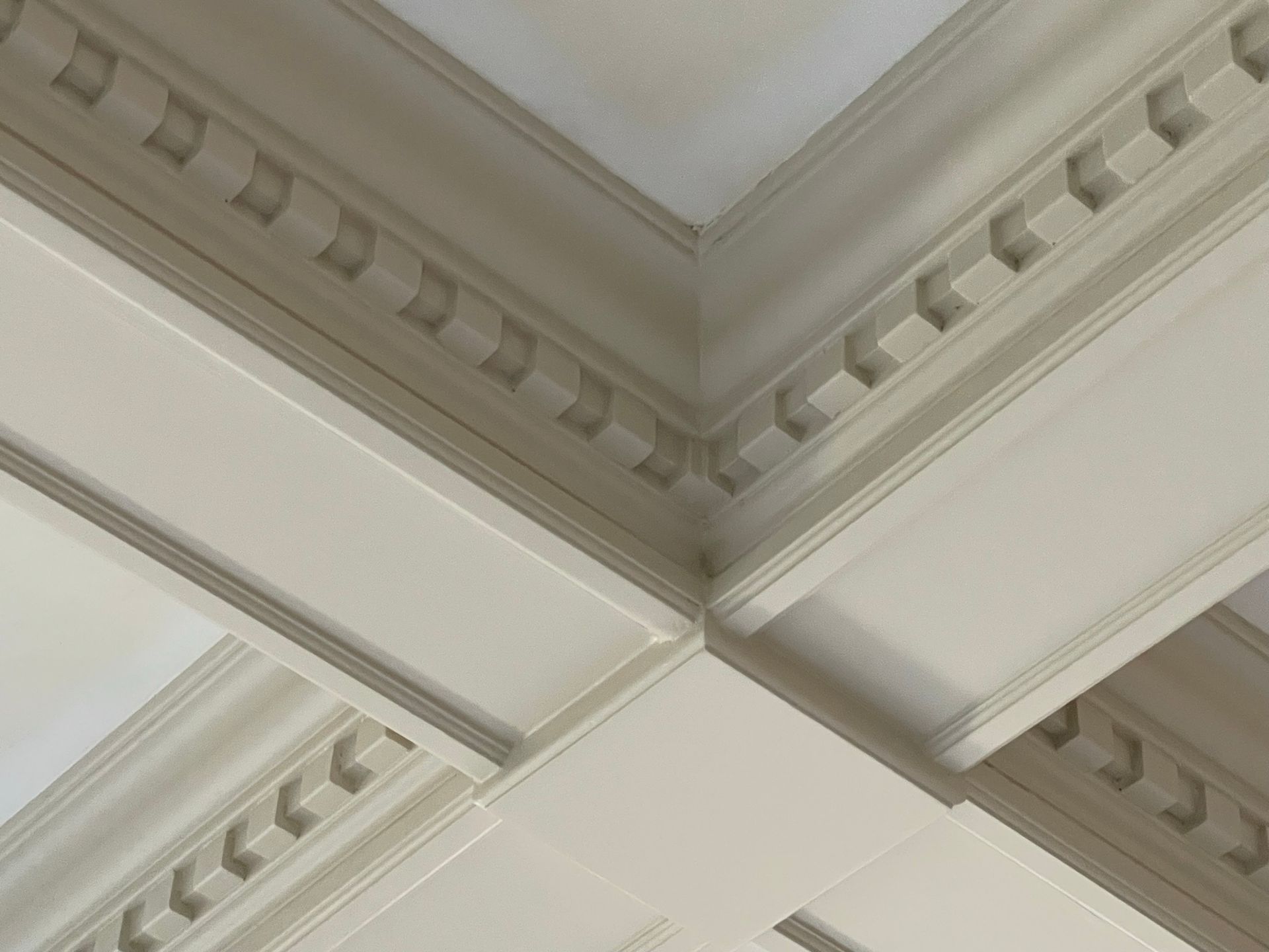 Close-up of white ceiling molding with decorative square patterns at the corners.