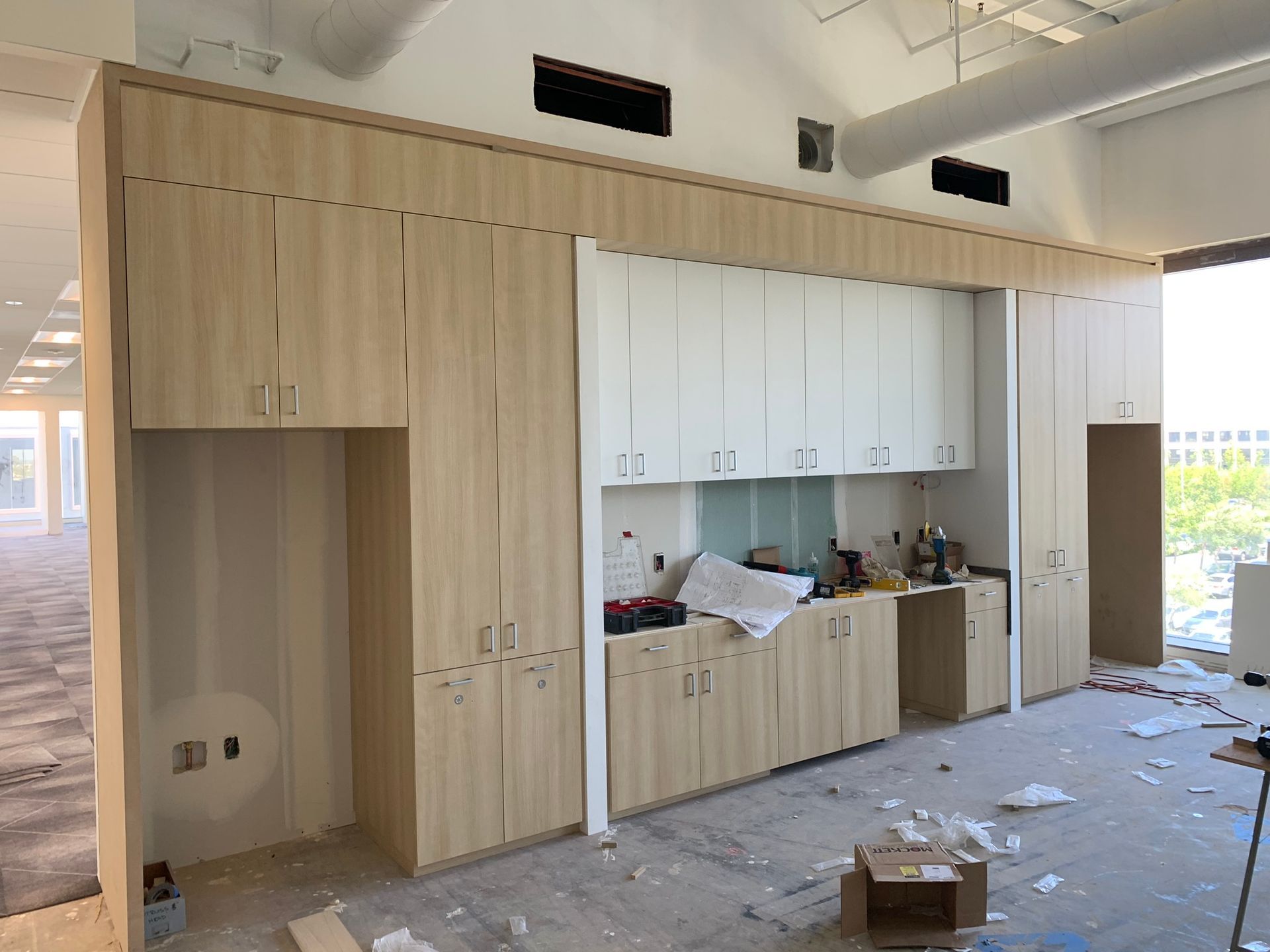 Construction site with light wood cabinets, white upper cabinets, and a partially finished kitchenette.