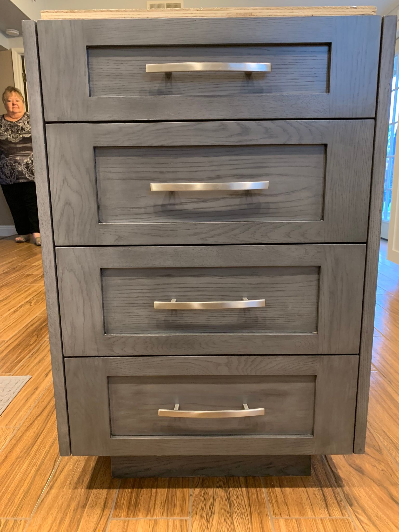 Gray cabinet with four drawers, each with a silver handle. A person stands to the left.