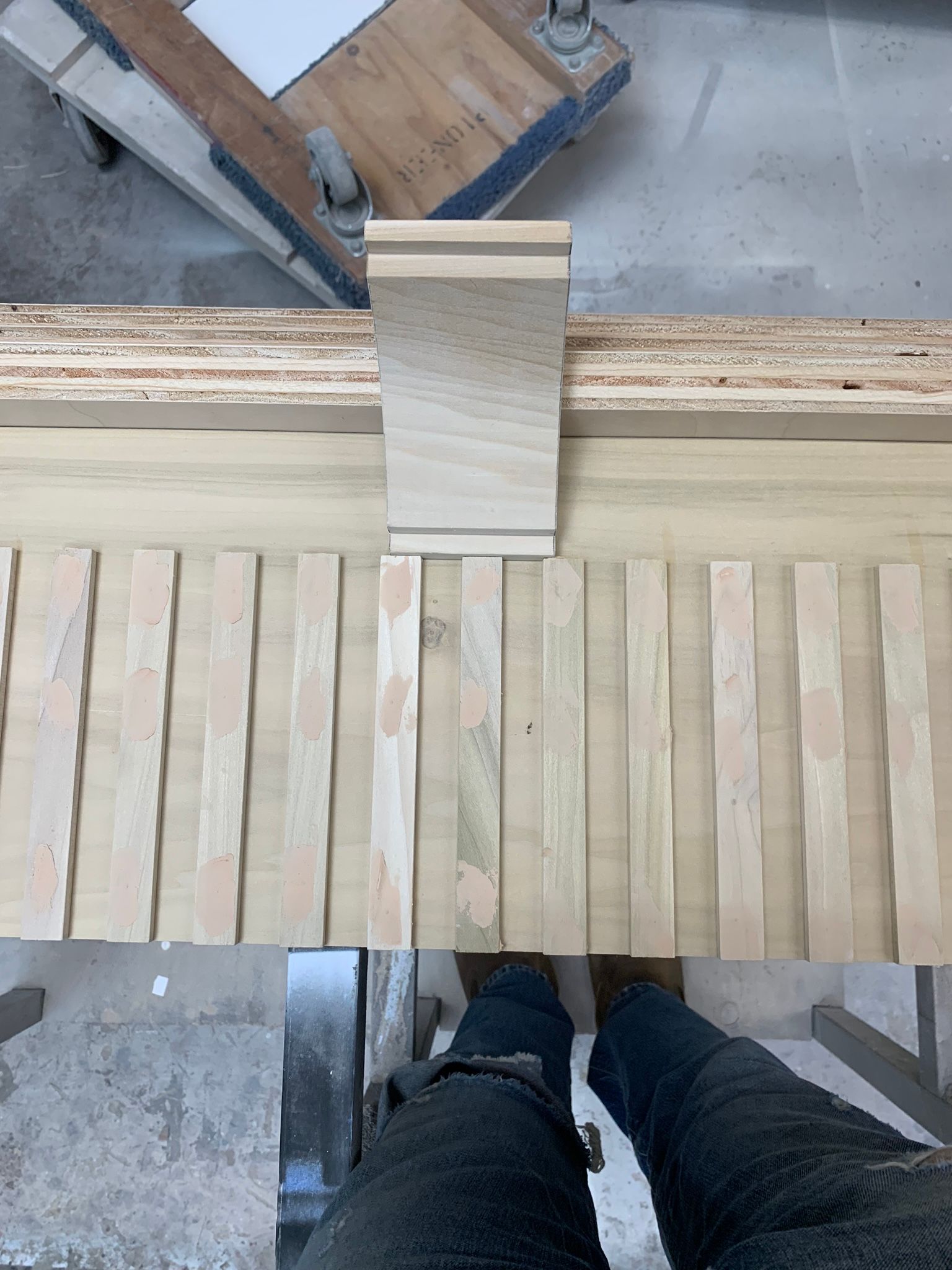 Woodworking: Person in jeans standing at a table saw, cutting wooden strips.