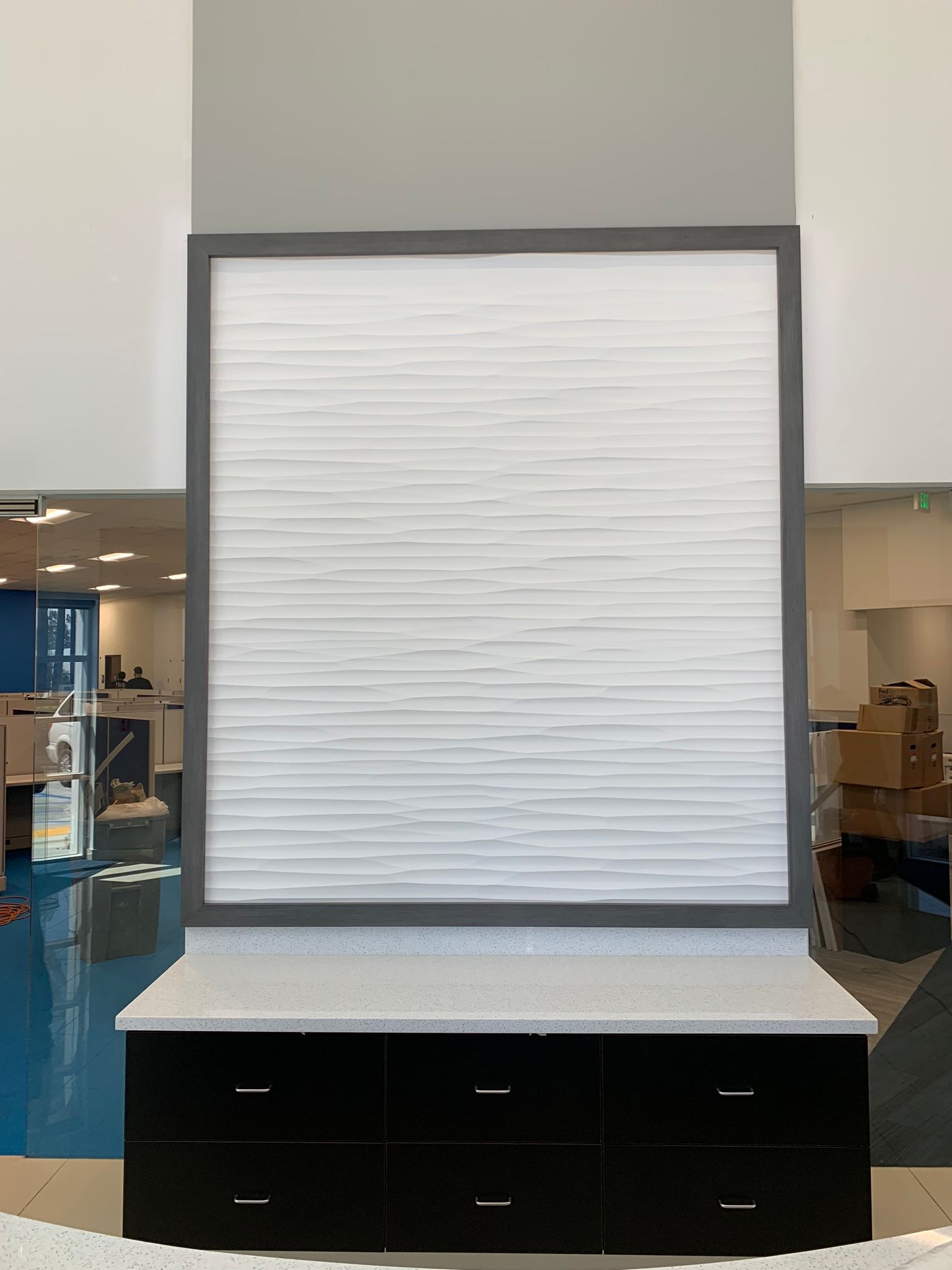 Black cabinets topped with speckled gray countertop, white textured panel framed in gray, against light and dark gray walls.