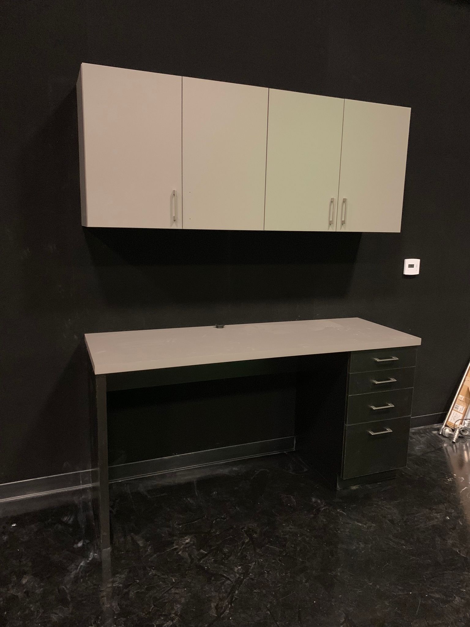 Gray desk and overhead cabinets against a black wall.