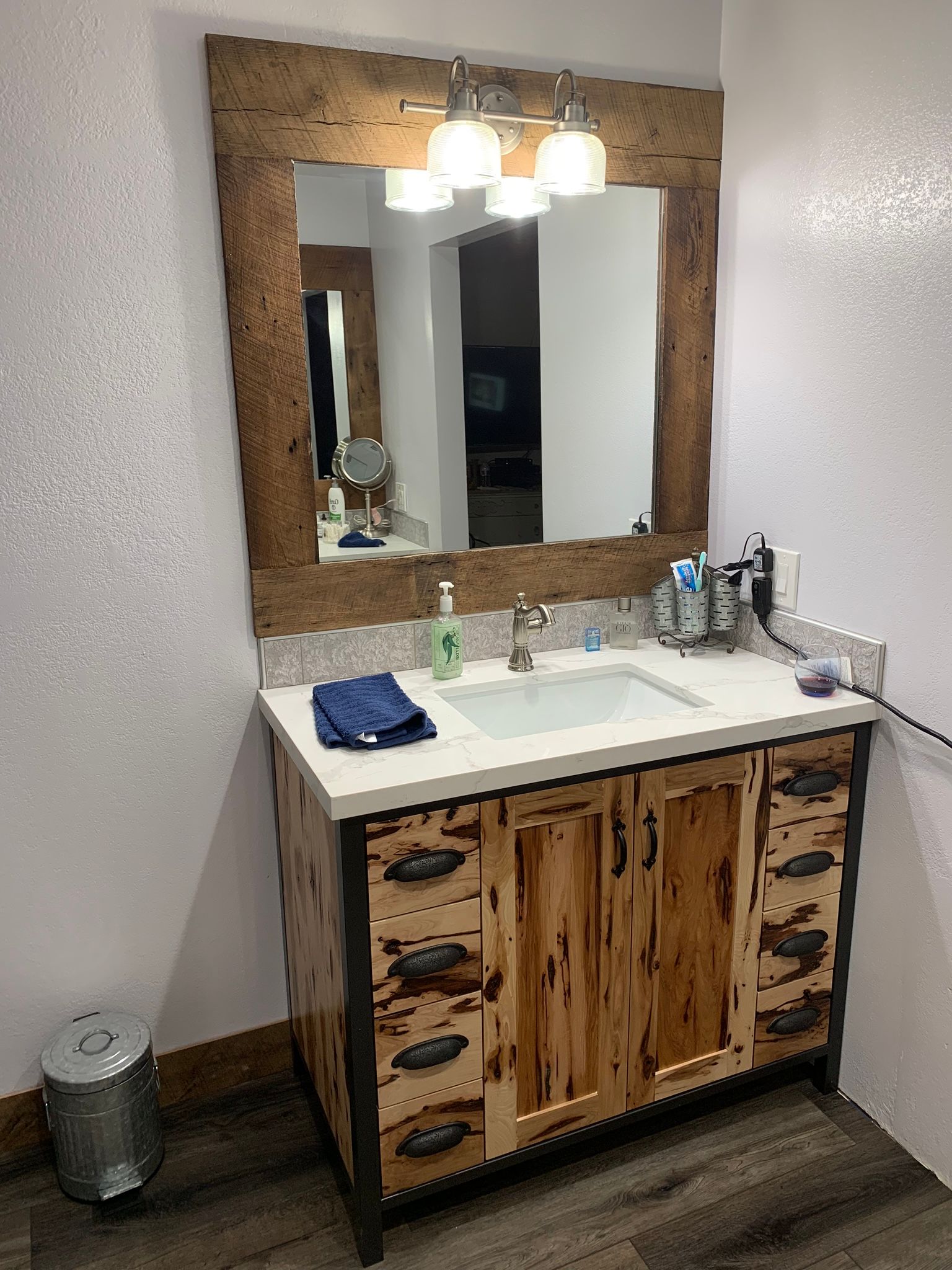 Bathroom vanity with wood cabinet, white countertop, mirror, and light fixture.