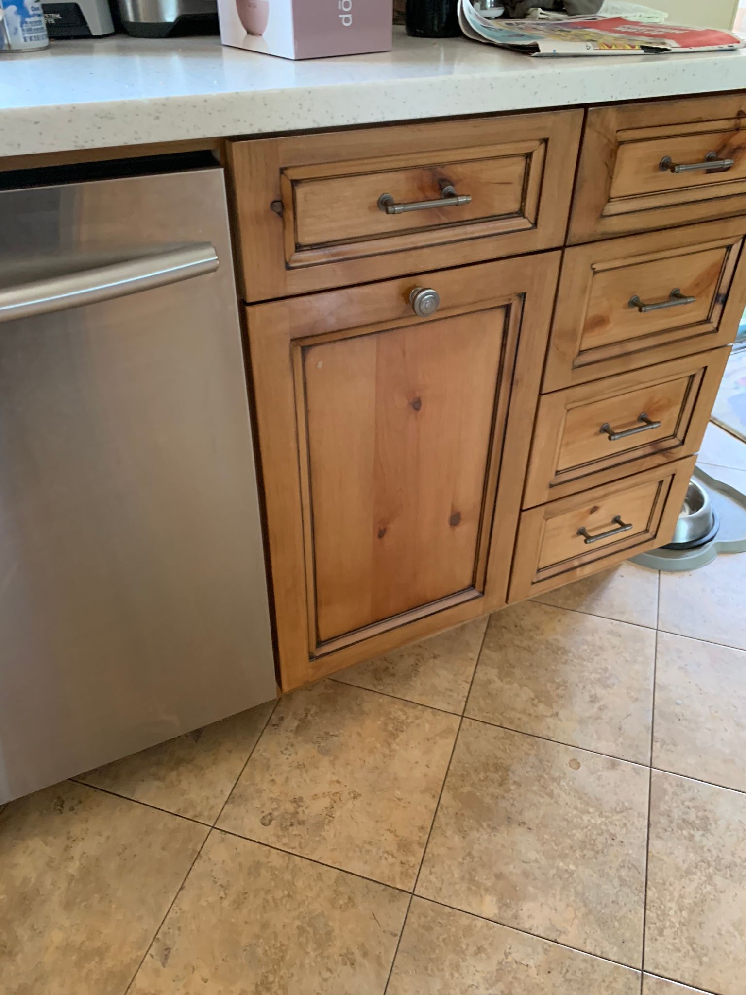 Stainless steel dishwasher next to light-brown wooden kitchen cabinets with drawers and countertop.