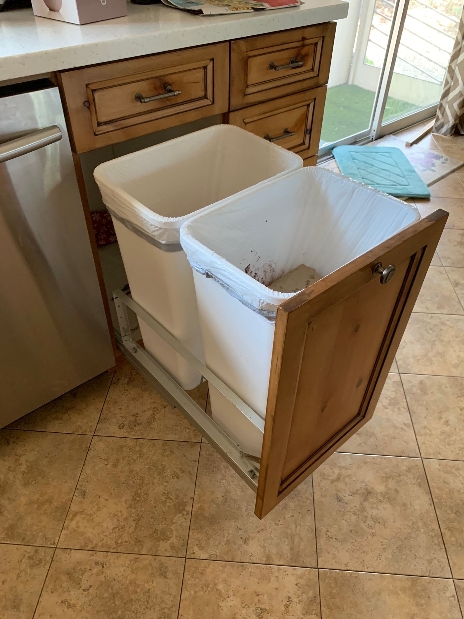 Pull-out kitchen cabinet with two white trash bins, one open and partially filled.