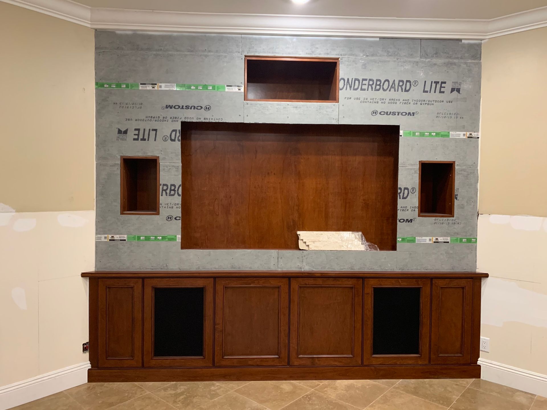 A dark wood entertainment center with built-in shelving and cabinets, mounted against a grey cement wall.