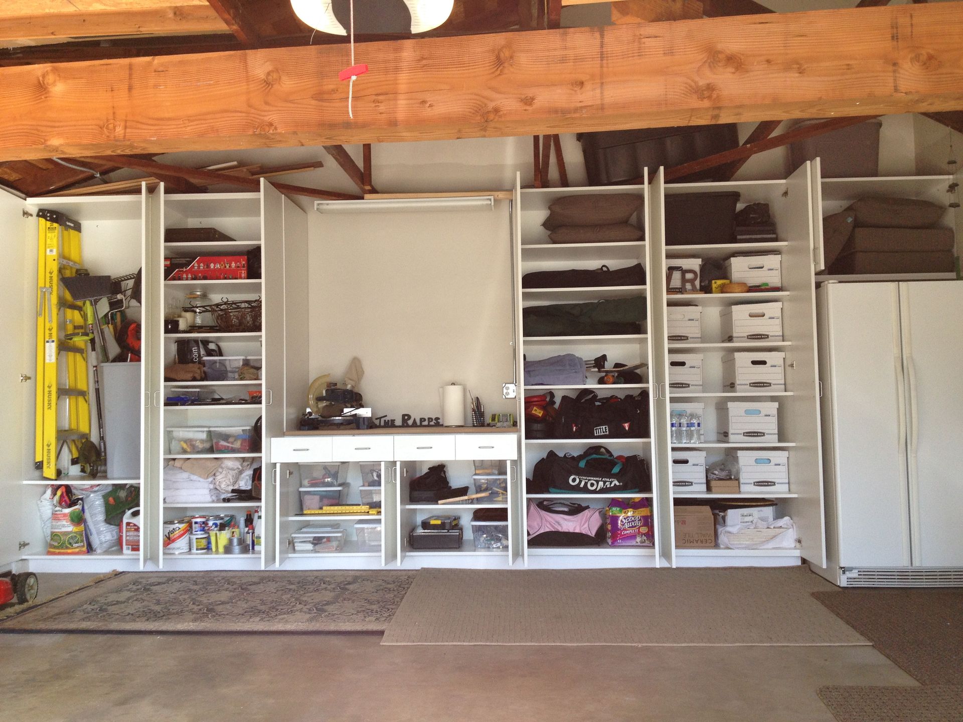 Garage with white cabinets, work surface, and various stored items.