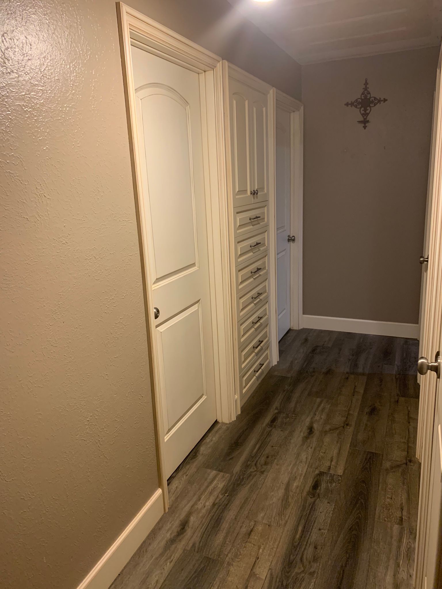 Narrow hallway with white cabinets, light wood flooring, and a door at the end.