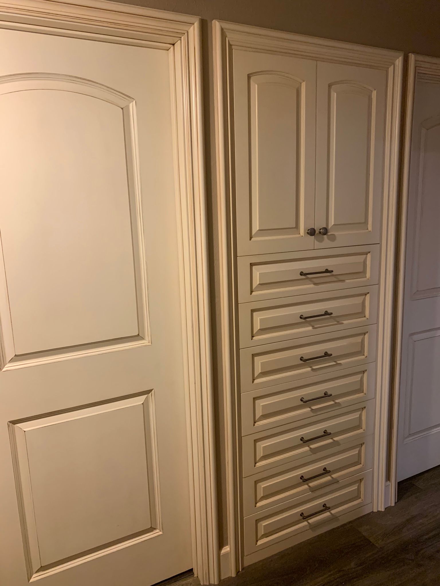 Built-in cabinet with drawers and two doors, all in a creamy white color, between two other doors.