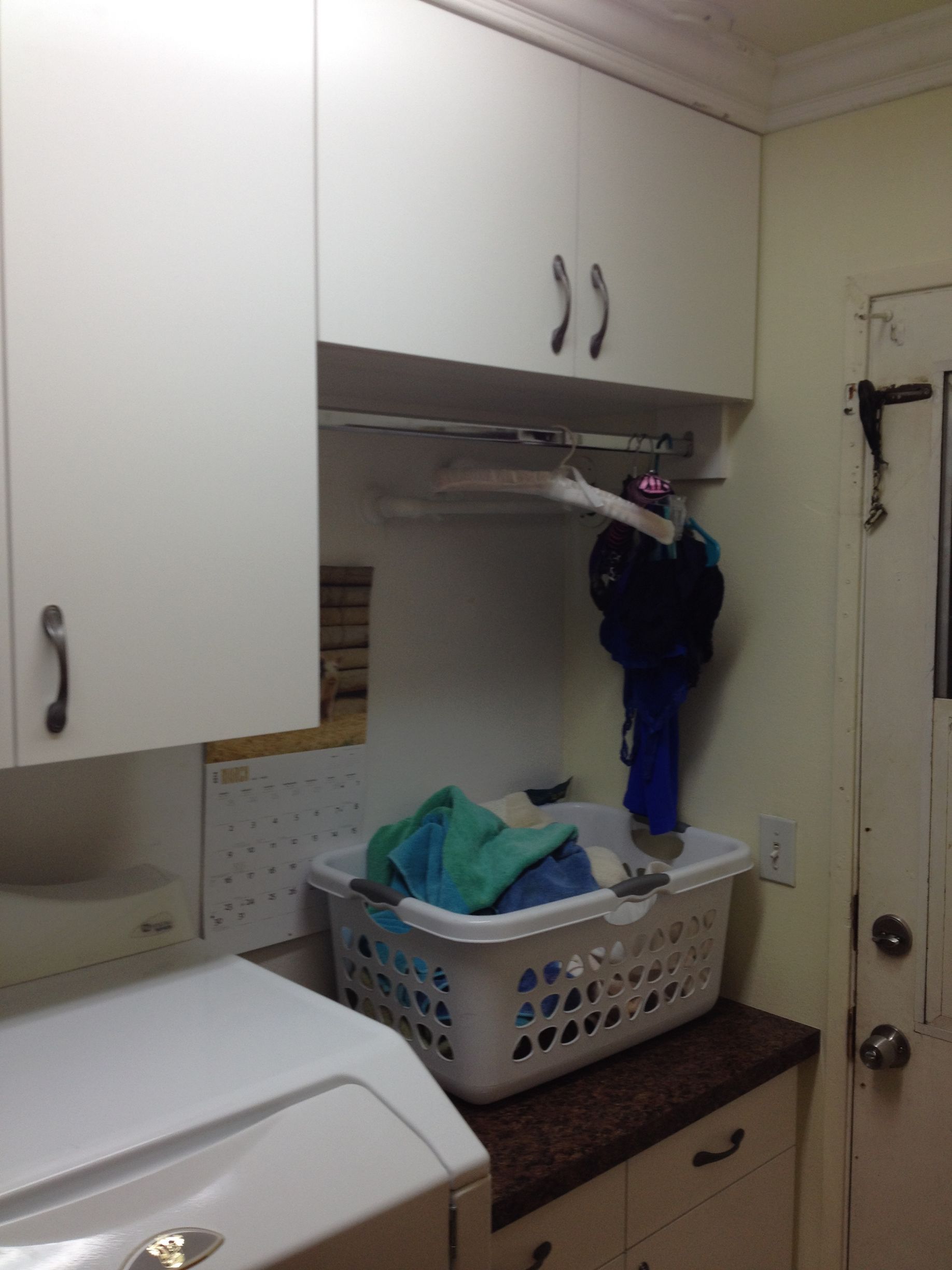 Laundry room with white cabinets, washer, clothes hanging, and laundry basket.