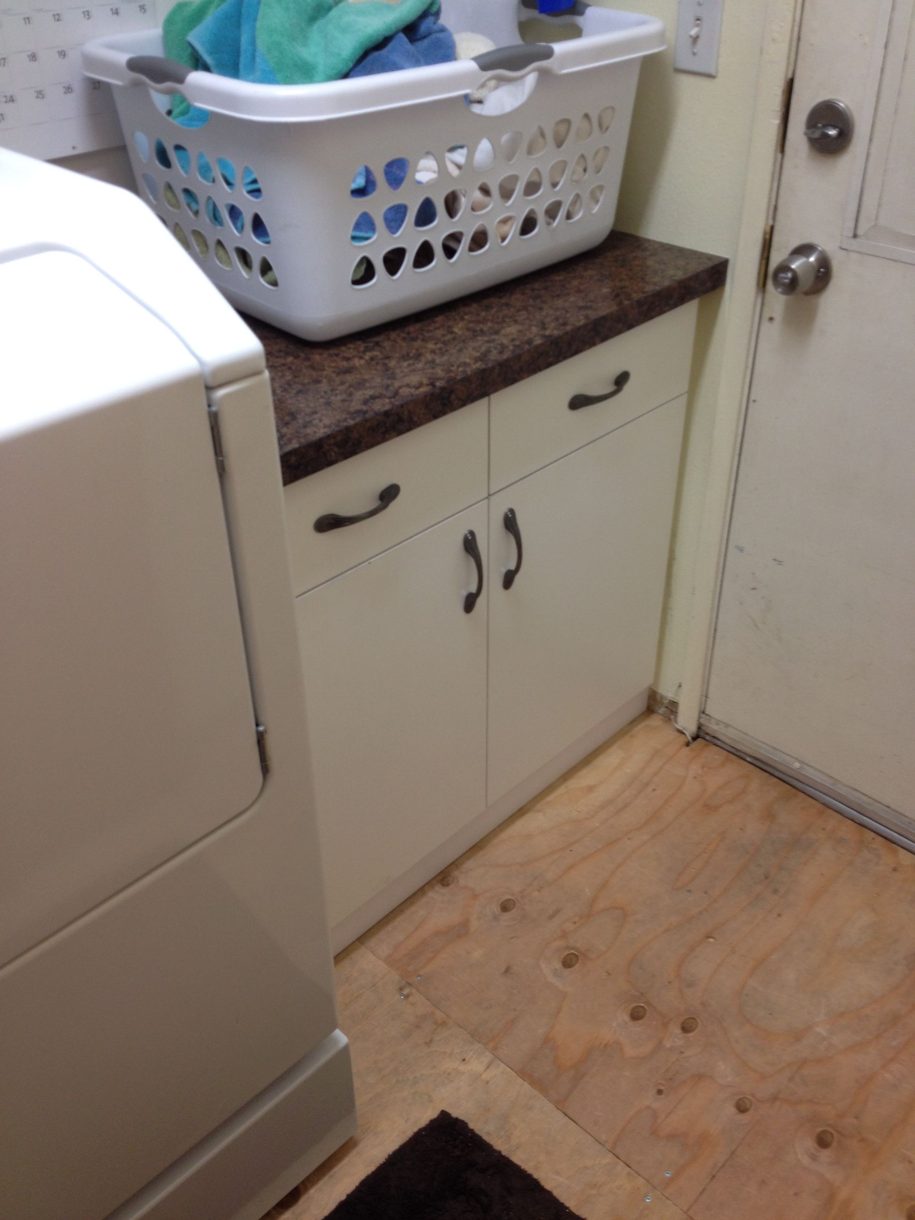 Laundry room with white cabinets, dark countertop, laundry basket, and washing machine.