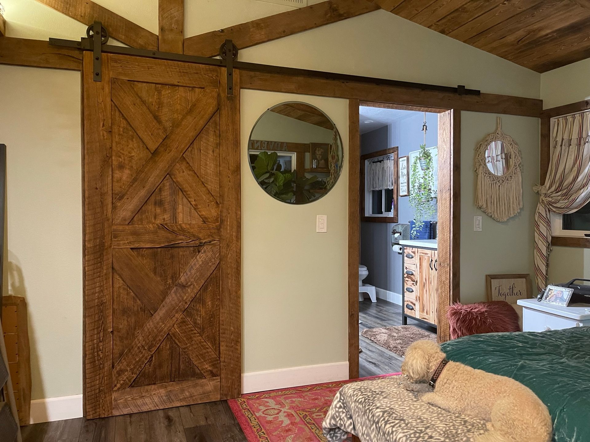 Barn door, open doorway to bathroom, dog on bed, round mirror.