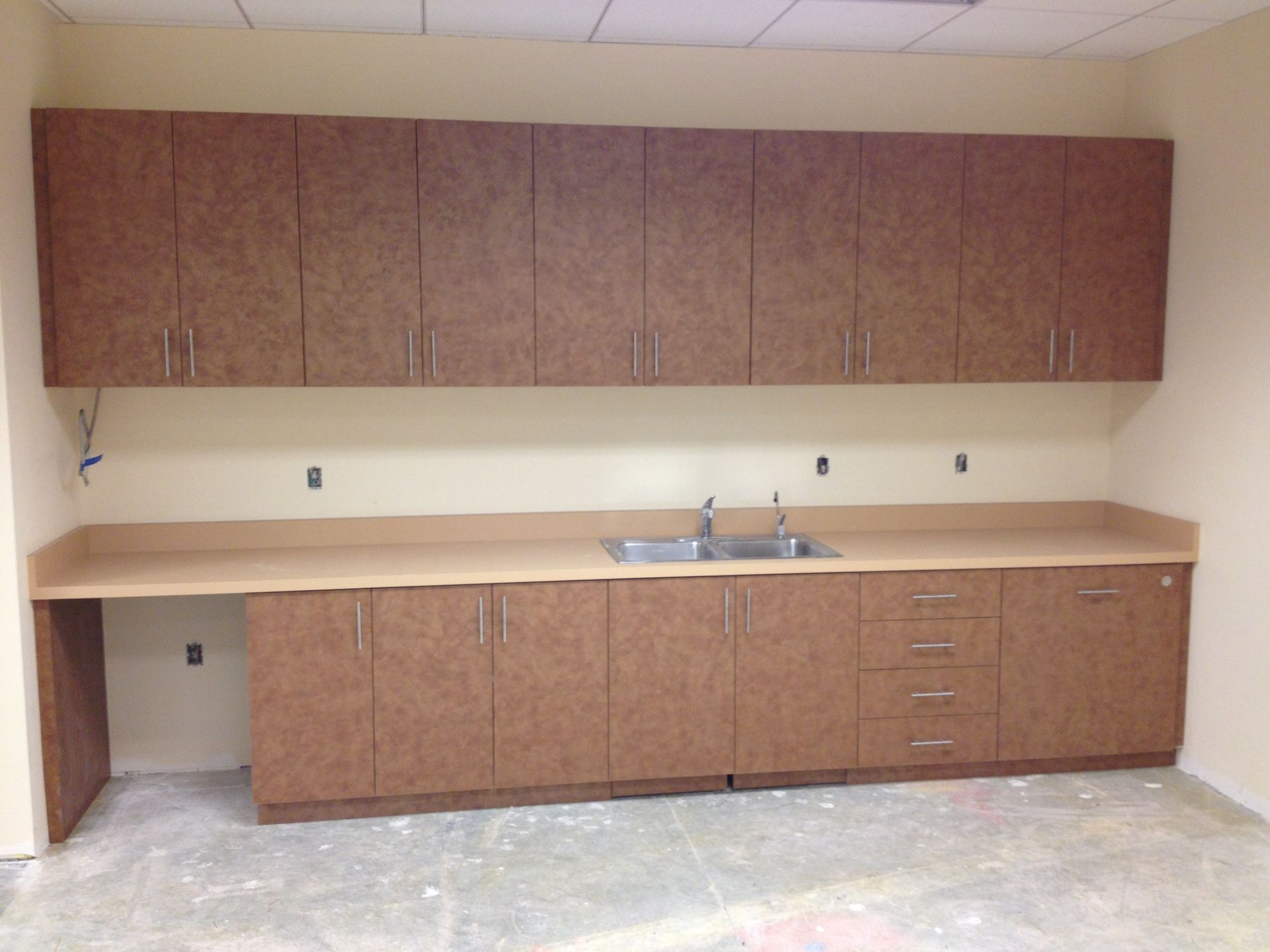Brown cabinets and counter with a sink, in an unfinished room.