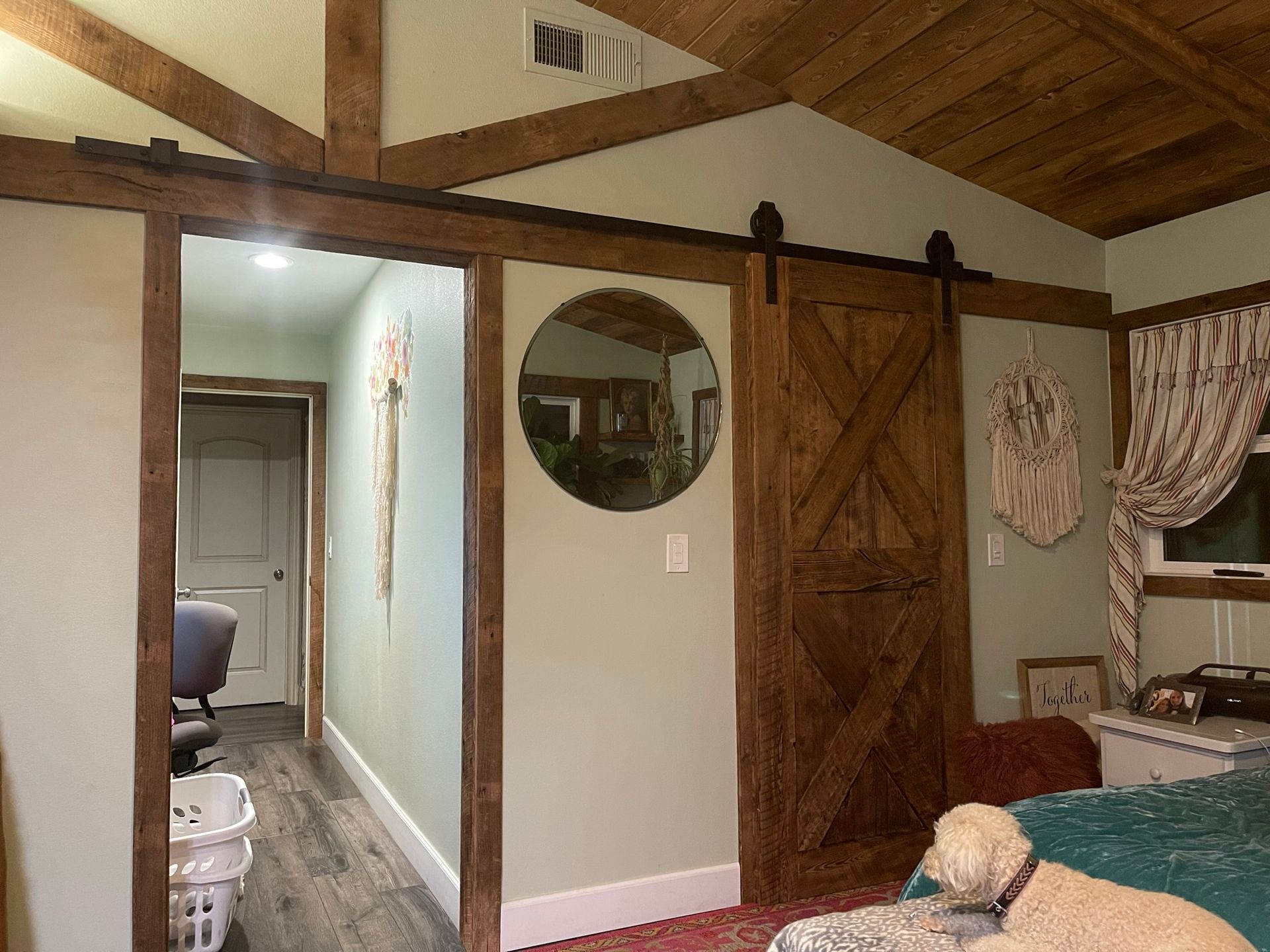 Bedroom with wooden accents, including a sliding barn door and ceiling beams. A dog sits on the bed.