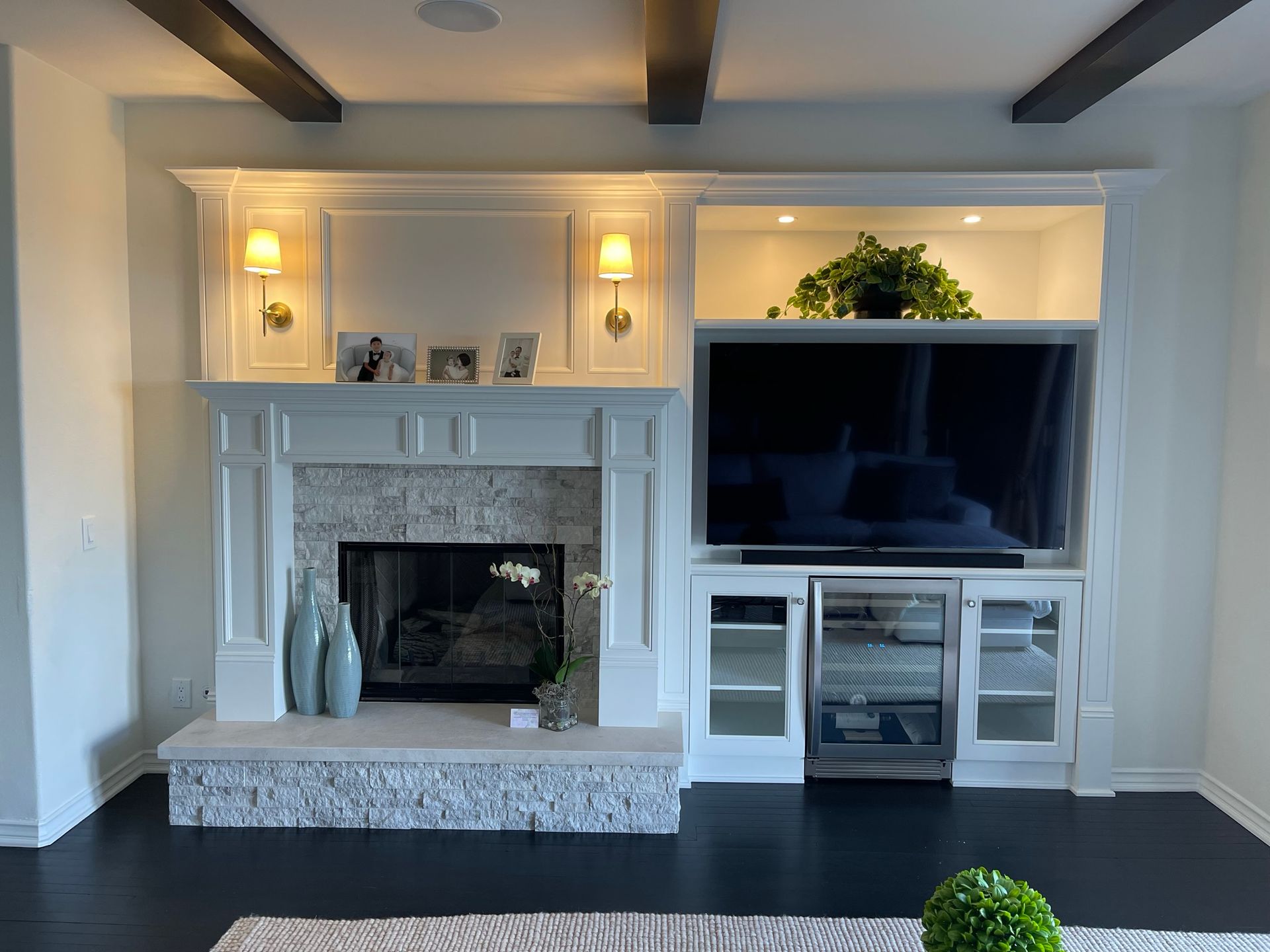 Fireplace with built-in TV and cabinets, white trim, stone surround. Dark wood floors, decorative vases, overhead lighting.