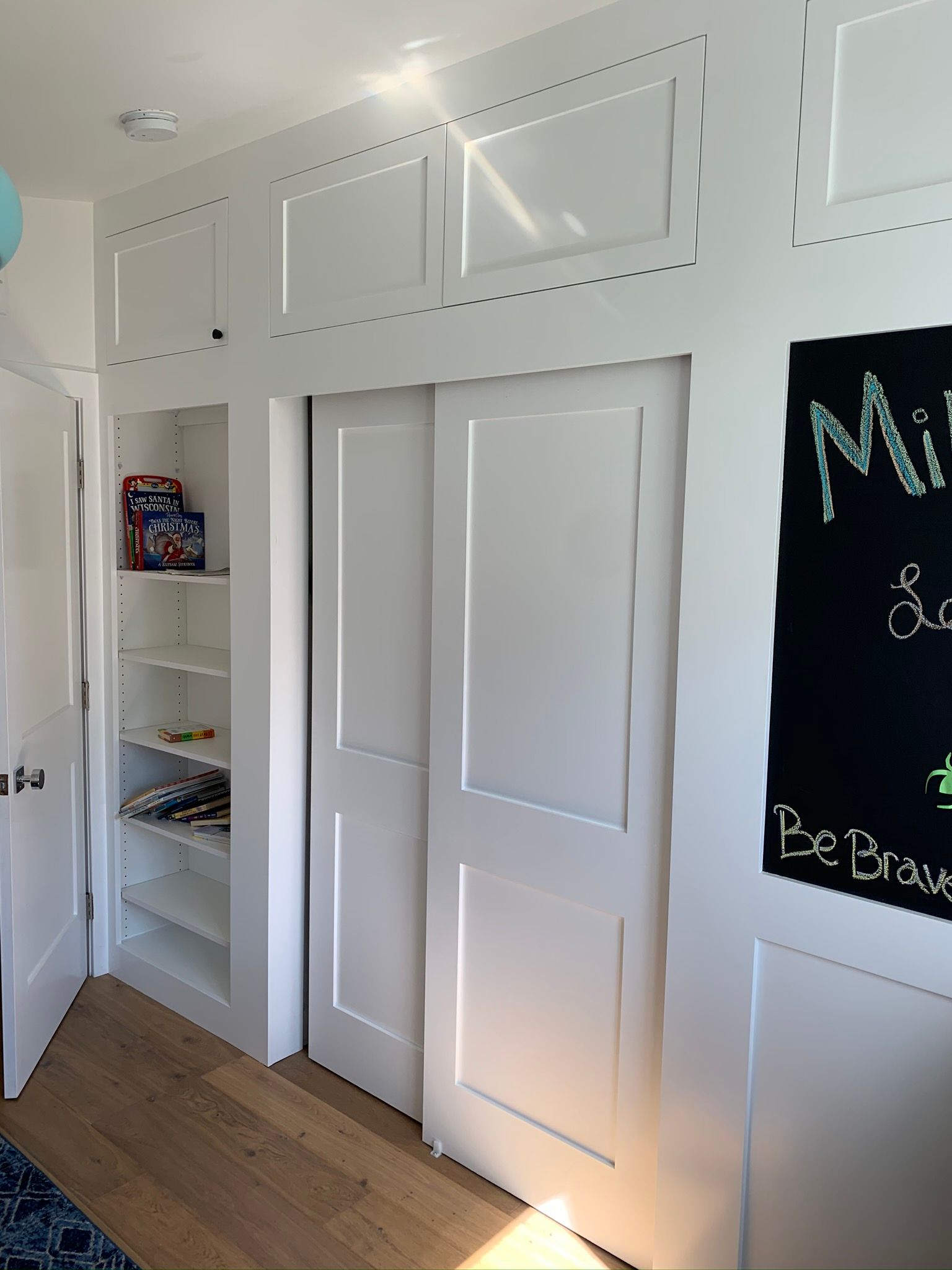White closet with sliding doors, built-in shelving, and chalkboard on the wall.