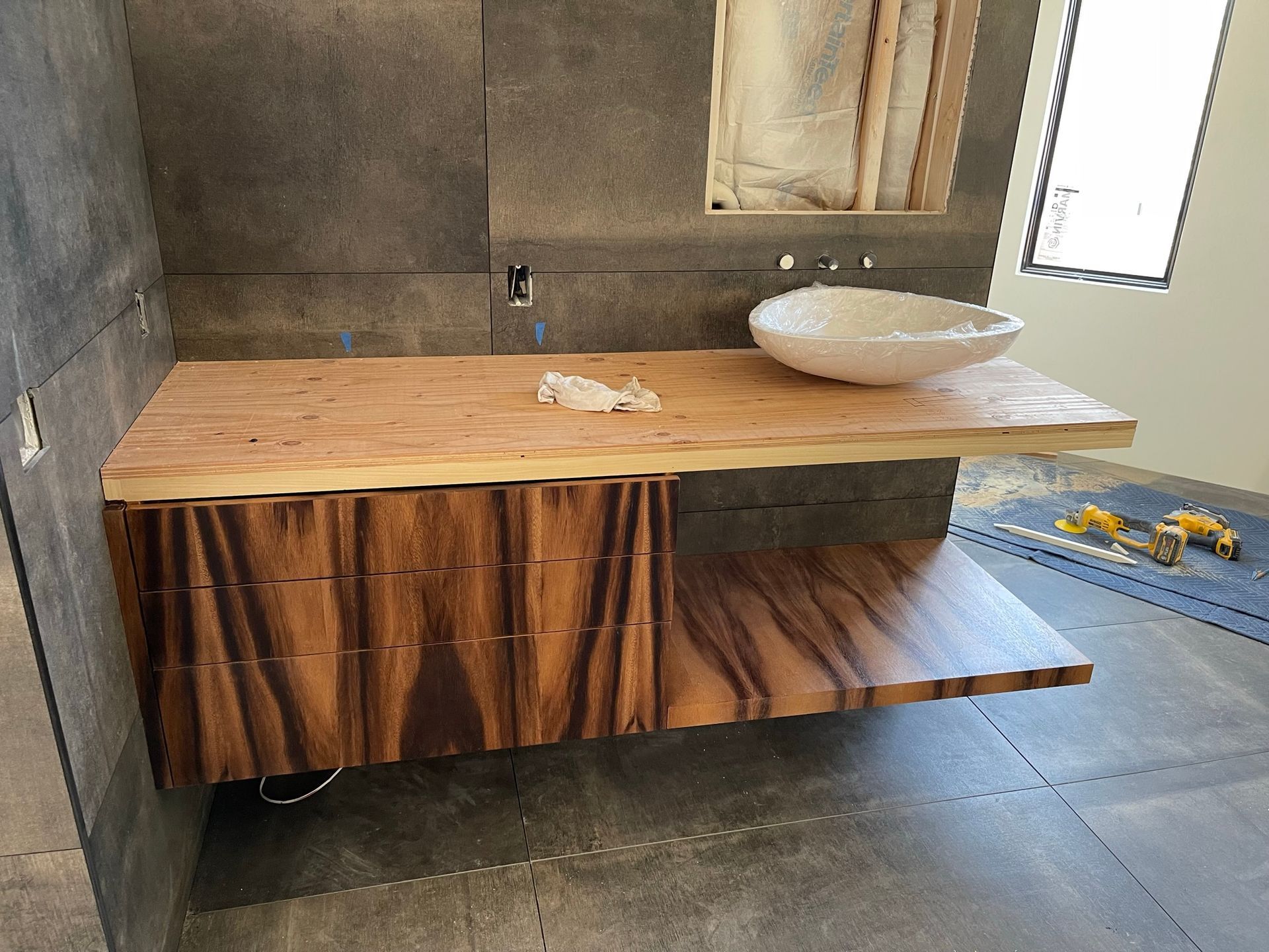 Floating wooden vanity with a vessel sink and drawers; under construction, unfinished bathroom.