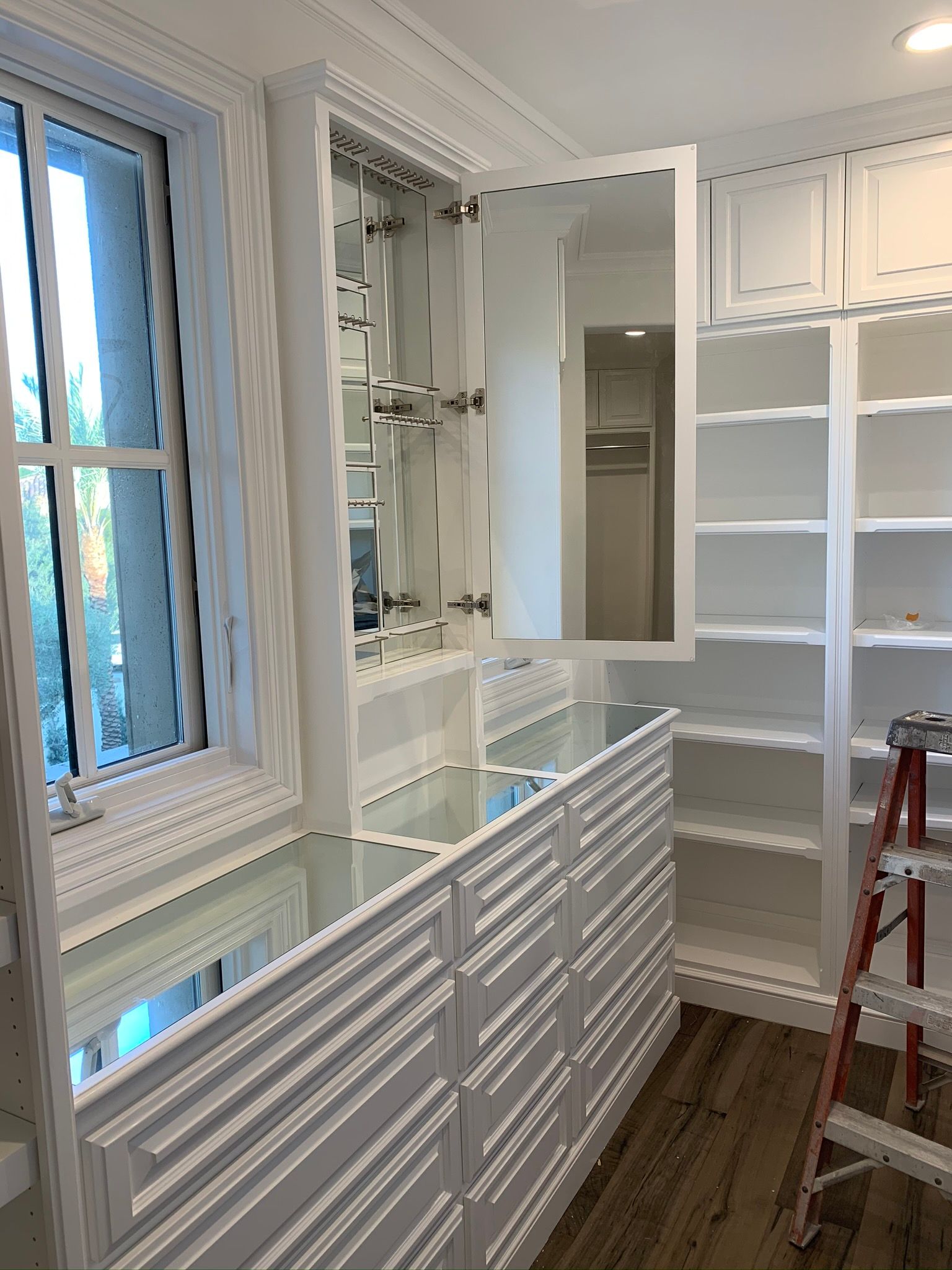 White custom built-in cabinetry with drawers, shelves, and a mirrored cabinet, beside a window.