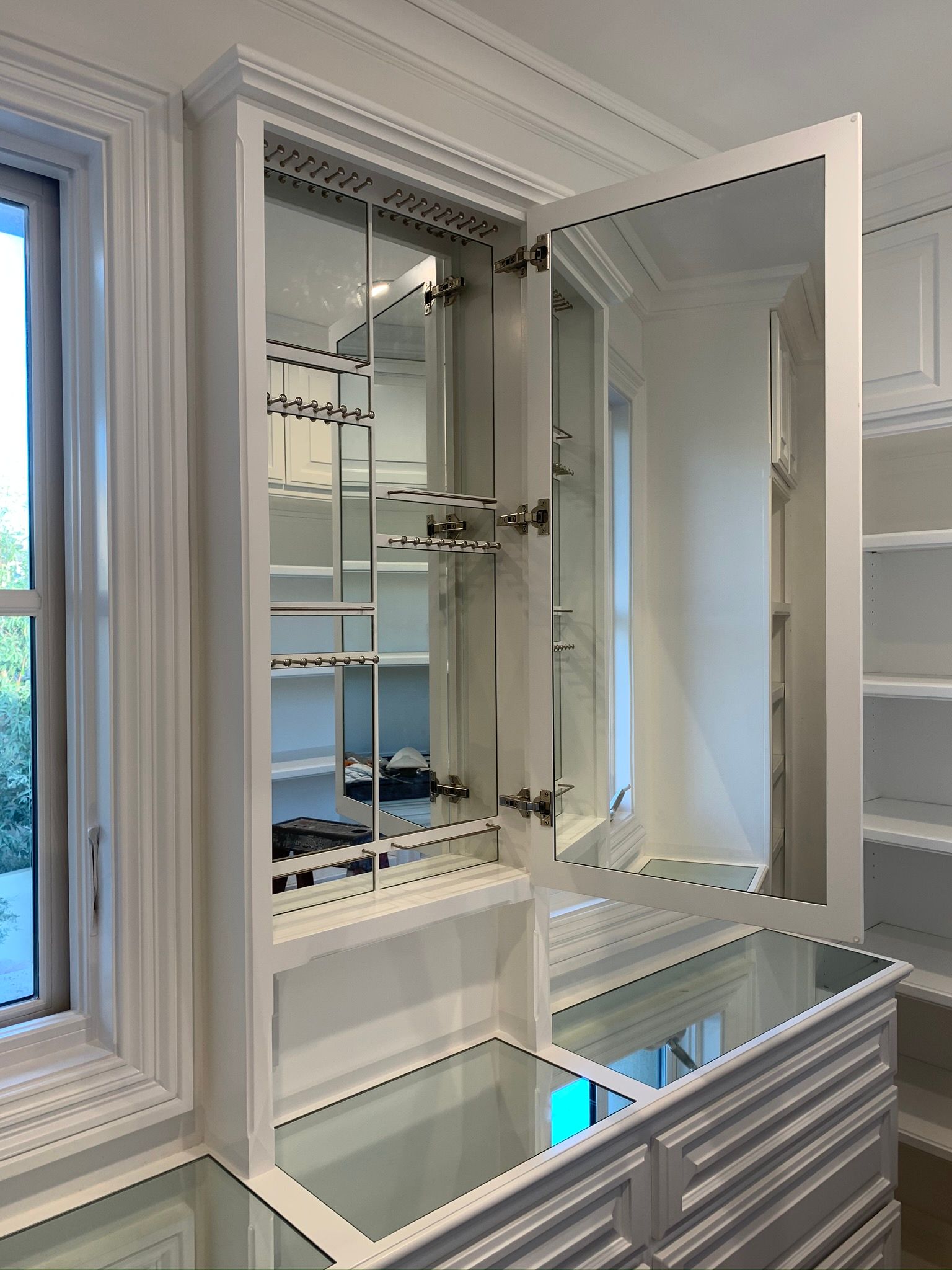 White cabinet with mirrored interior, open doors, built-in shelves, and a mirrored countertop.