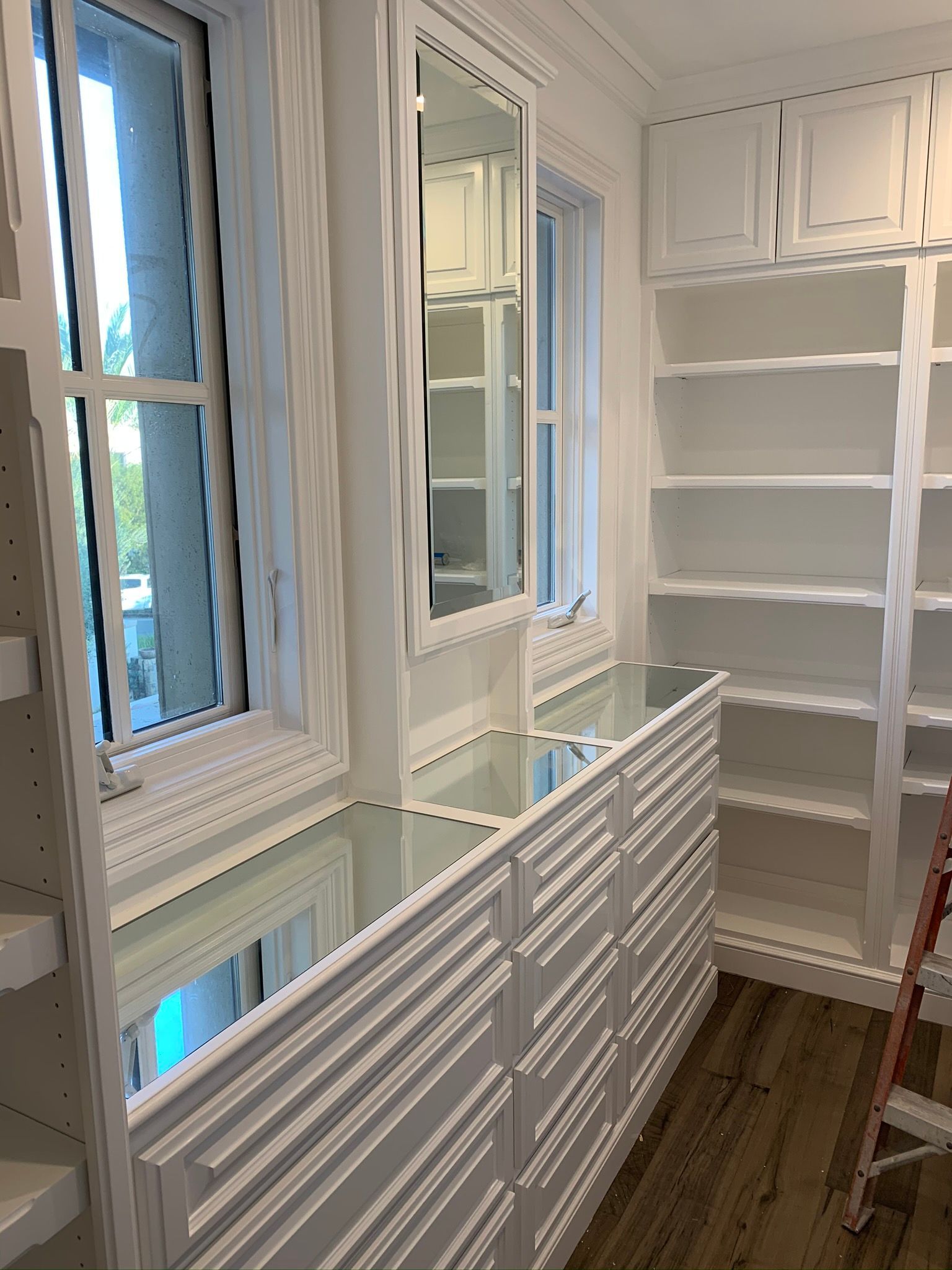 White built-in closet with drawers, shelves, windows, and a tall mirror.