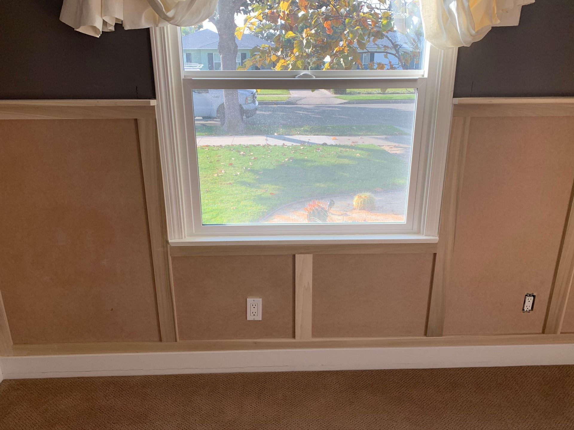 Room interior with a window and wainscoting. Beige walls, window with white trim, and brown carpet.