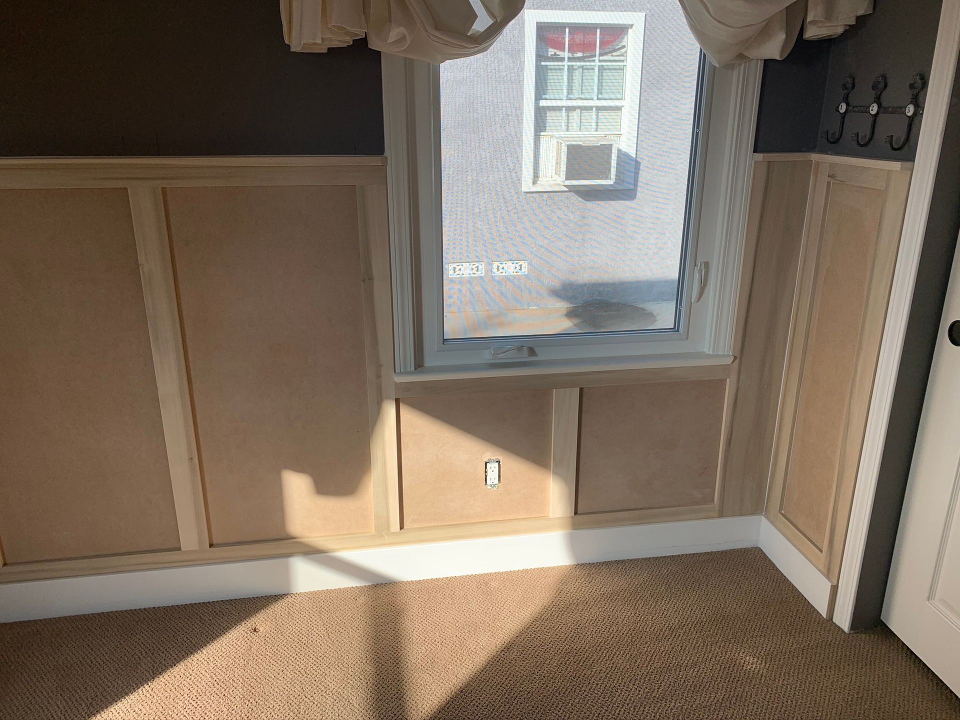 Bedroom interior with beige paneling, window, and carpet. Light shines in, illuminating the space.