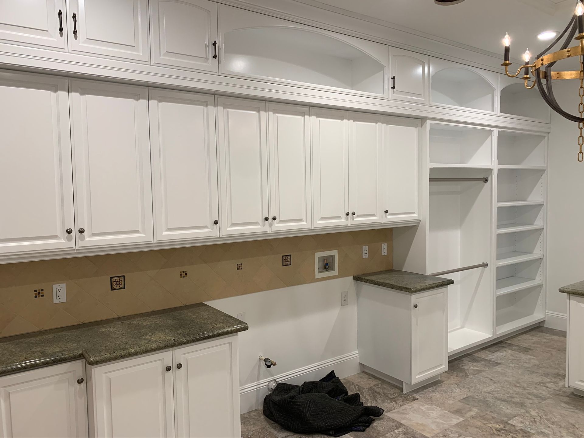 White cabinetry in a laundry room with a granite countertop, open shelving, and a chandelier.