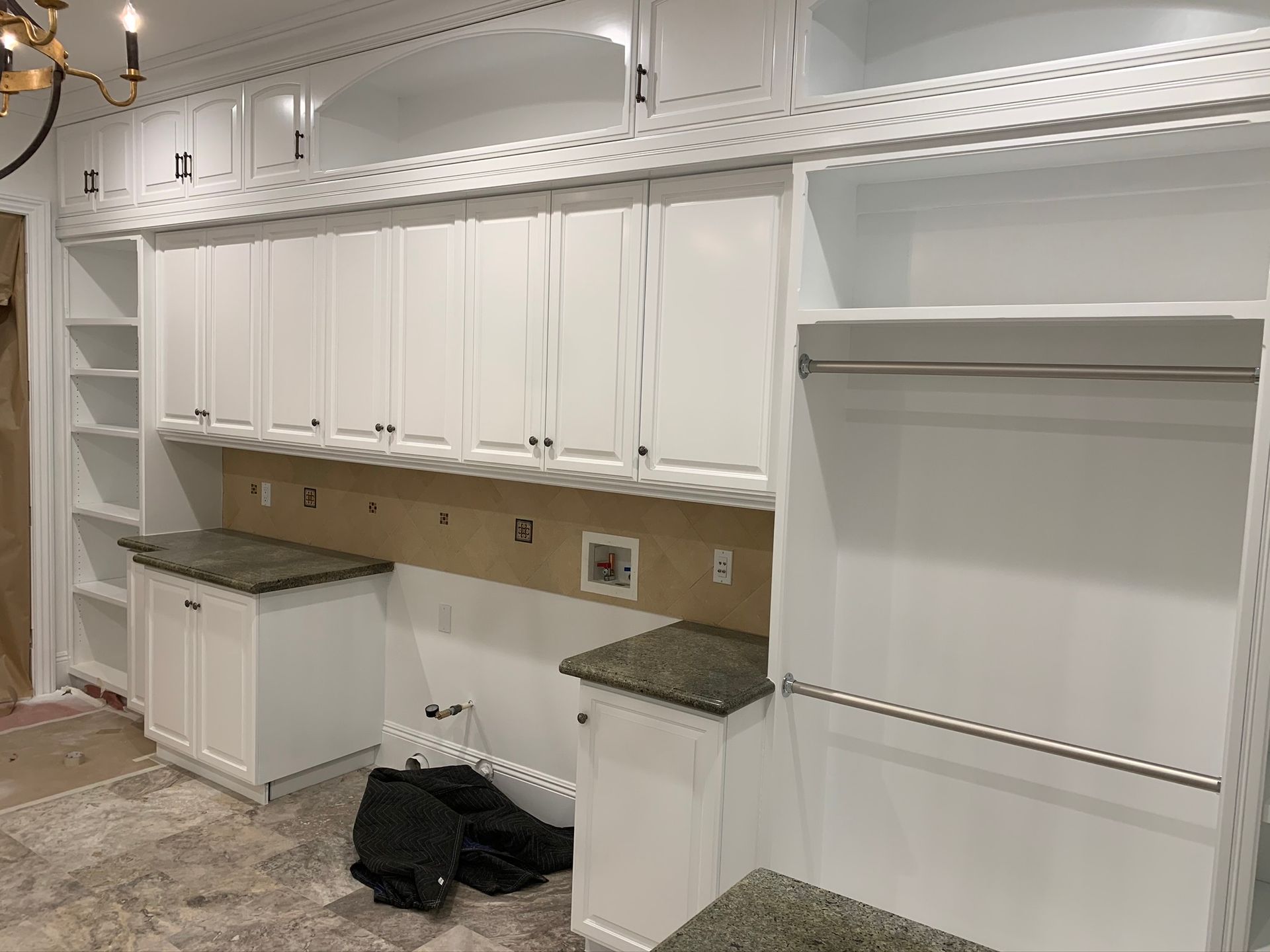 White custom laundry room cabinets with granite countertops and a hanging rod.