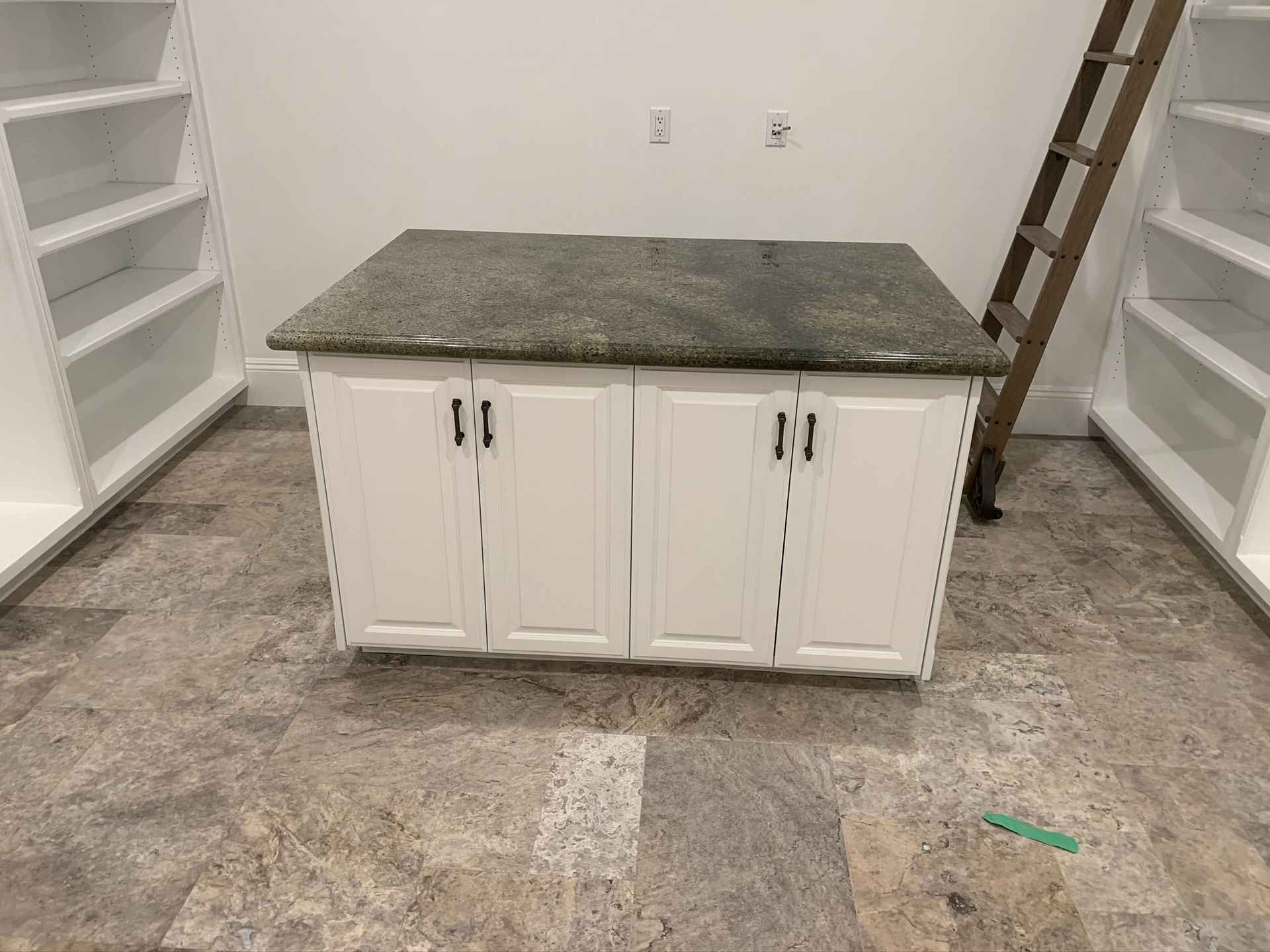White cabinet with granite countertop in room with shelves, near ladder.