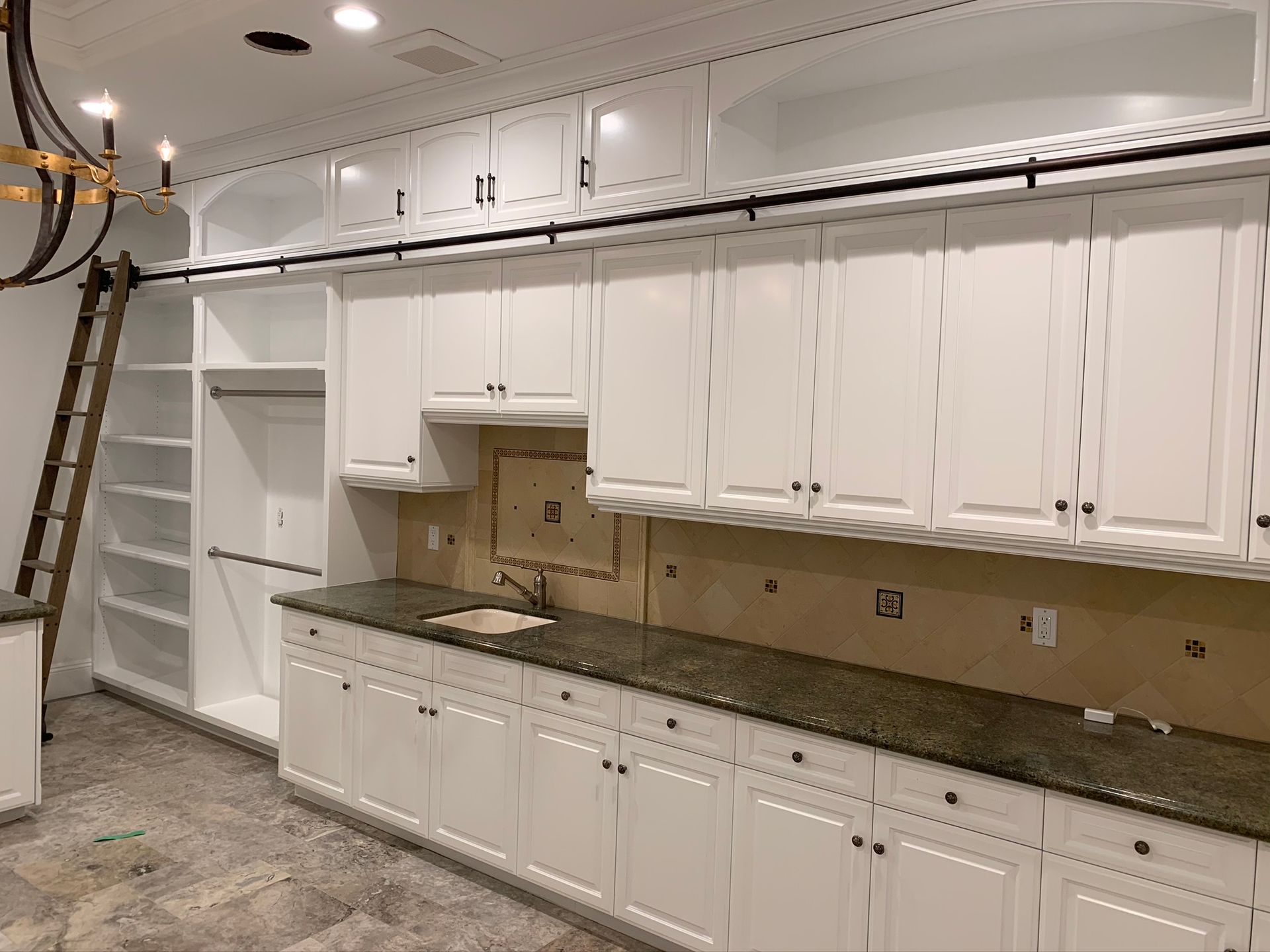 White kitchen cabinets with granite countertop; unfinished backsplash, ladder on the left.