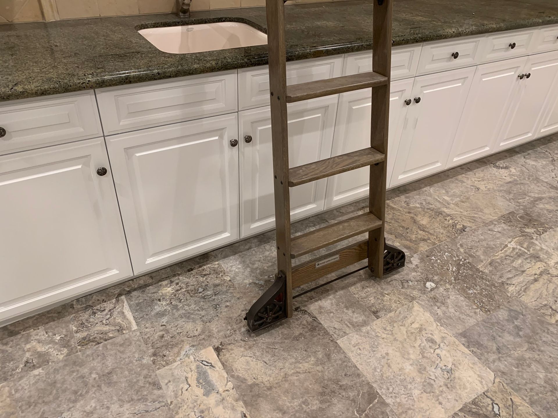Wooden step ladder leaning against white cabinets and a granite countertop.