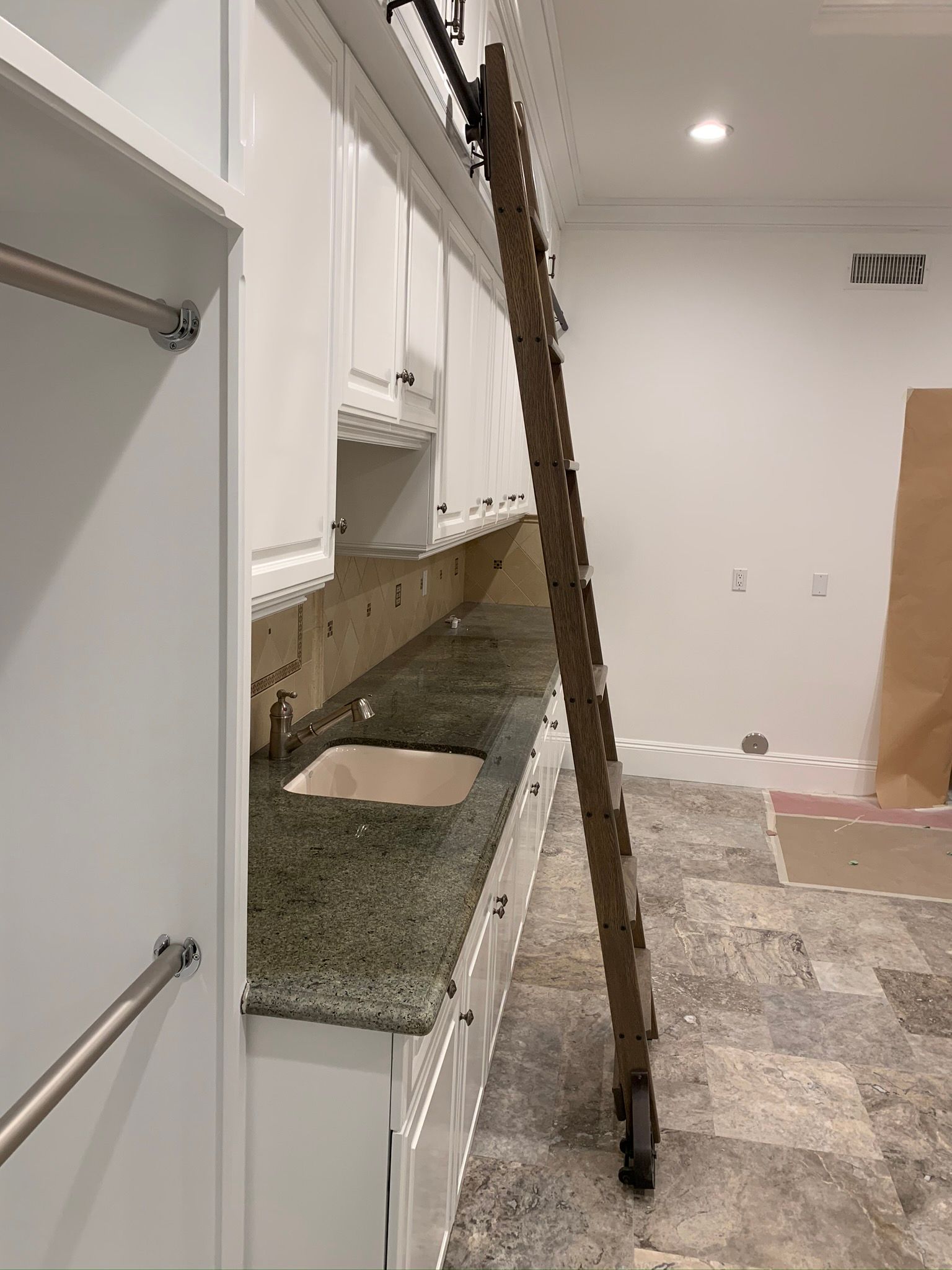 A kitchen with white cabinets, granite countertop, and a rolling ladder for accessing upper cabinets.