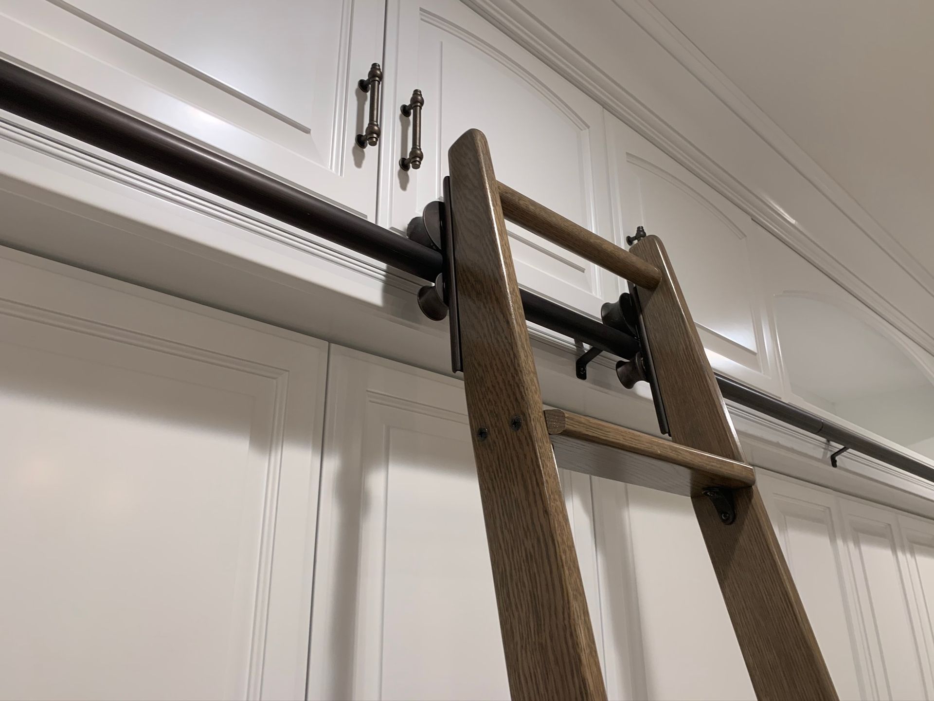 Wooden library ladder on a dark rod track in front of white cabinets.