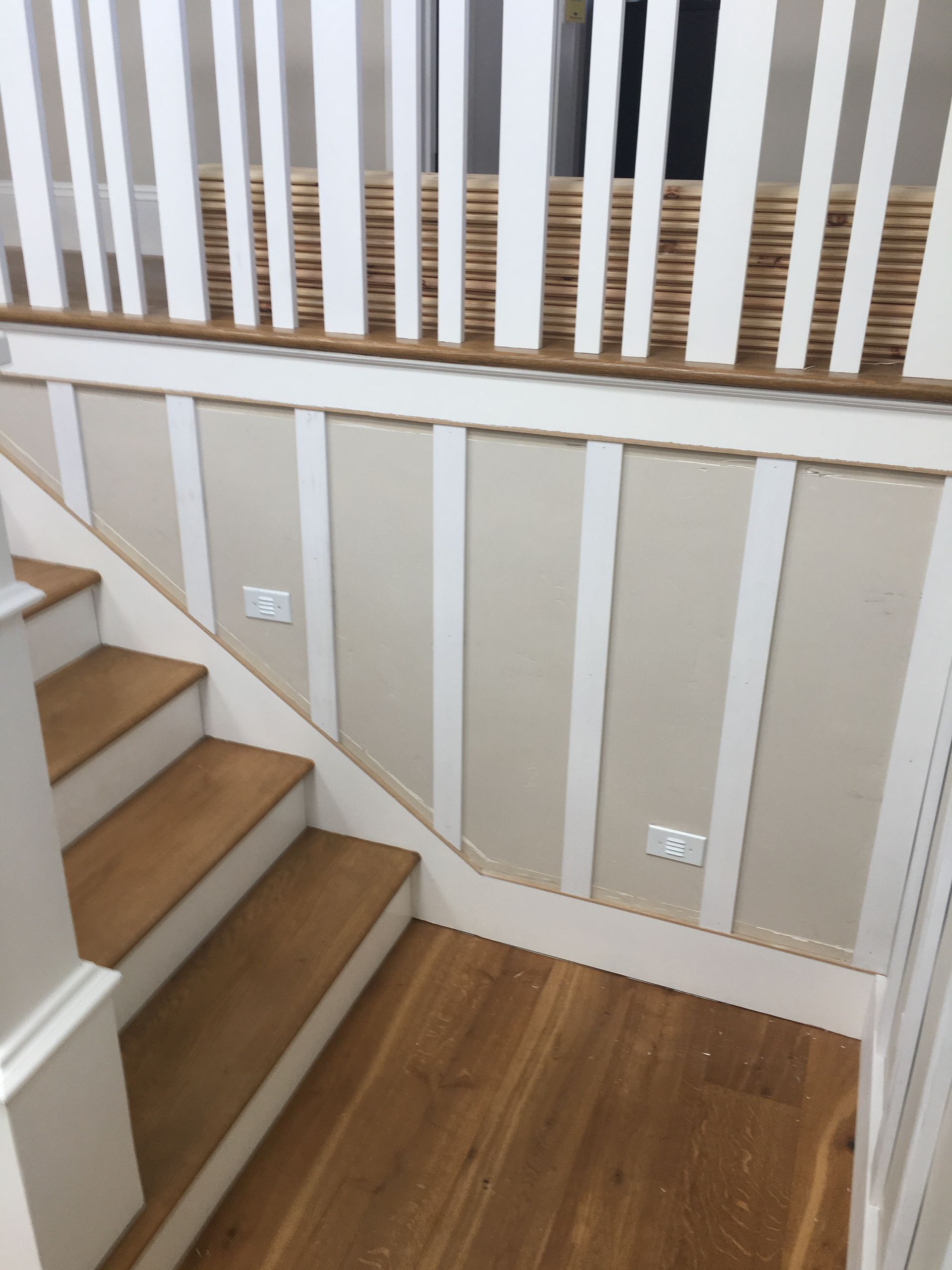 Wooden staircase with white banister, vertical white wall panels, and two electrical outlets.
