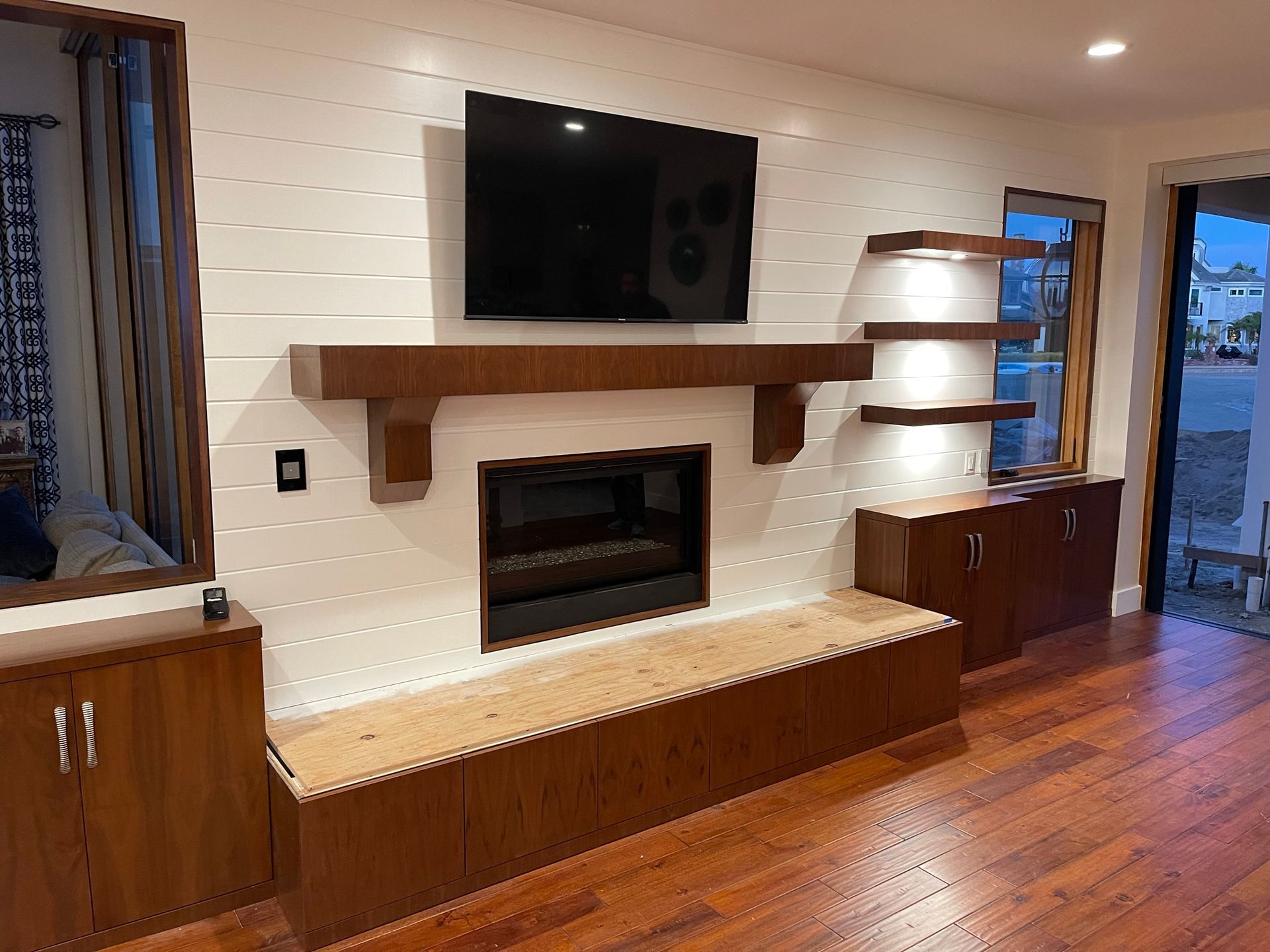 Fireplace with mounted TV, wooden shelves, and cabinets against a white shiplap wall.